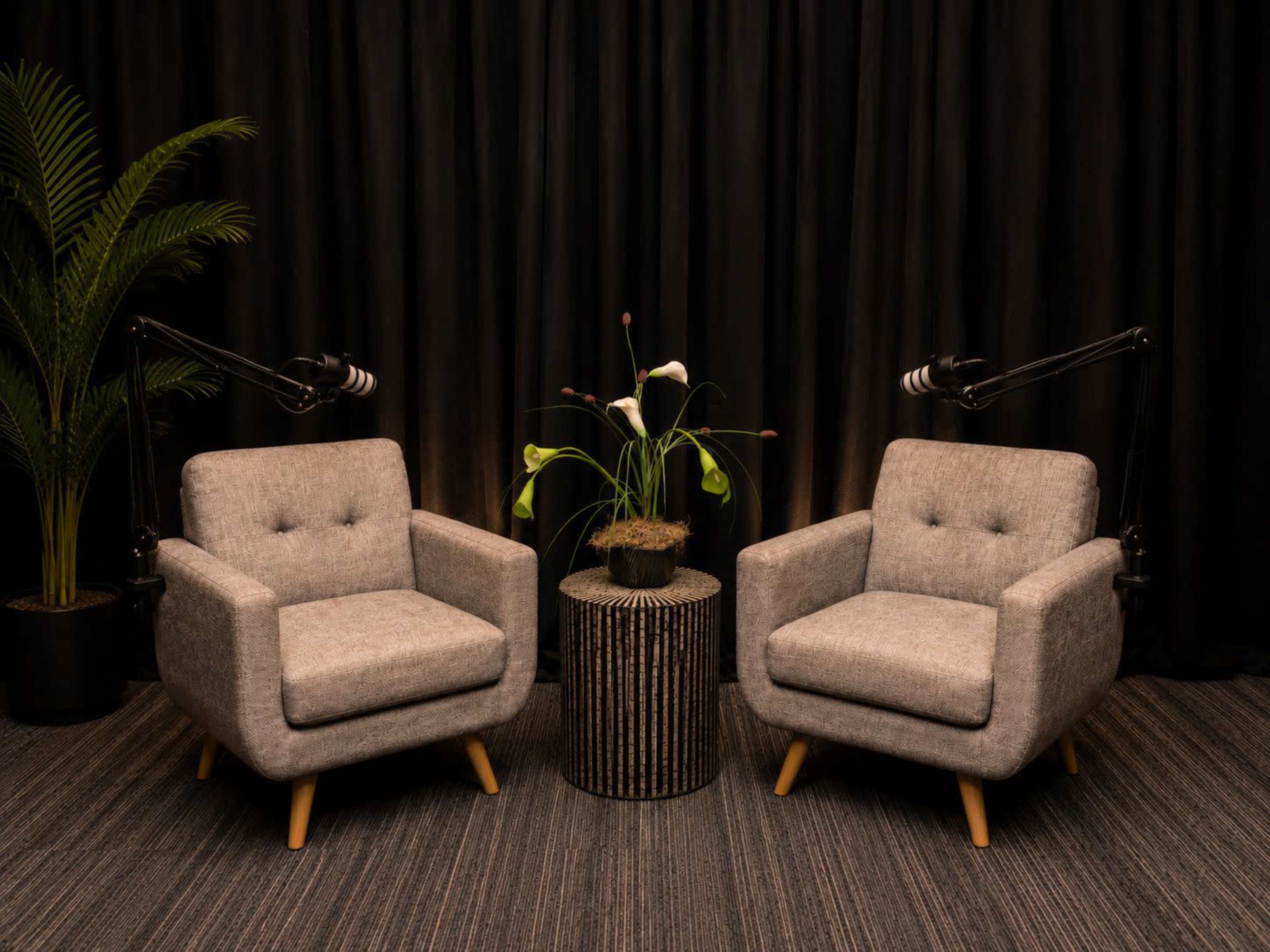 The image features two gray armchairs positioned opposite each other, with a small round table and a potted plant in between, against a backdrop of black curtains.