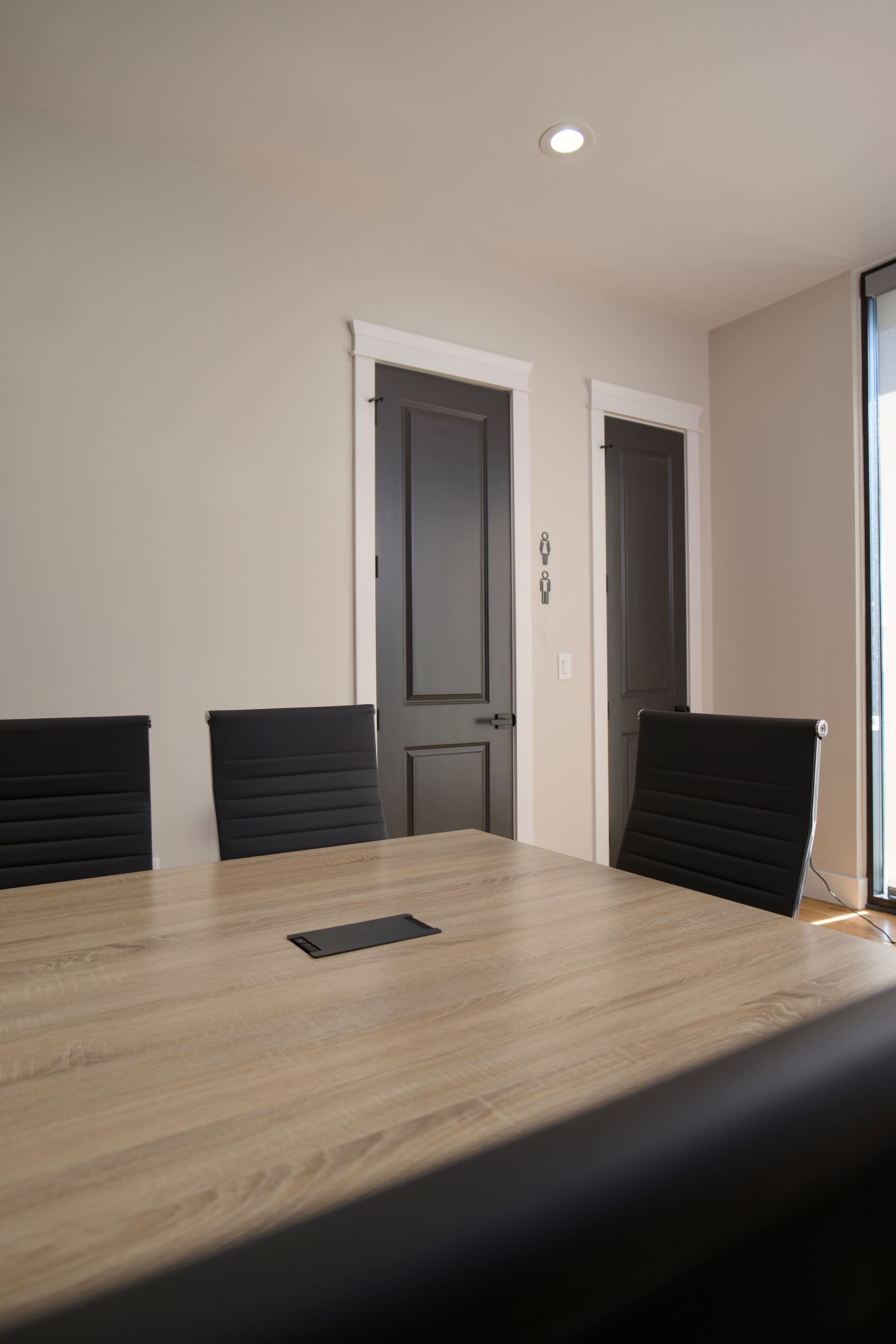 The image shows a conference room with a wooden table and several black chairs, adjacent to two closed doors.