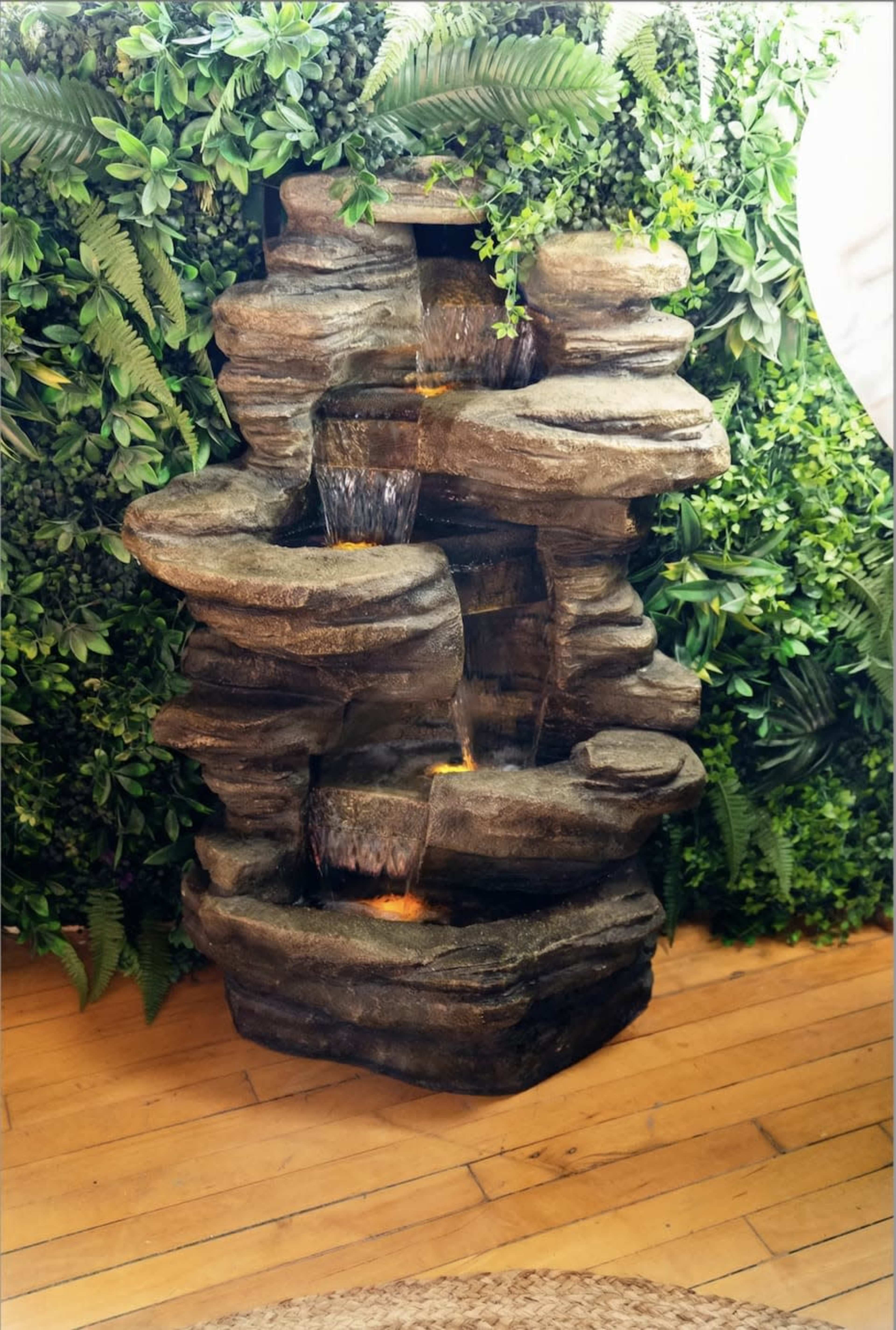 A decorative stone water fountain with multiple tiers is surrounded by lush green foliage.