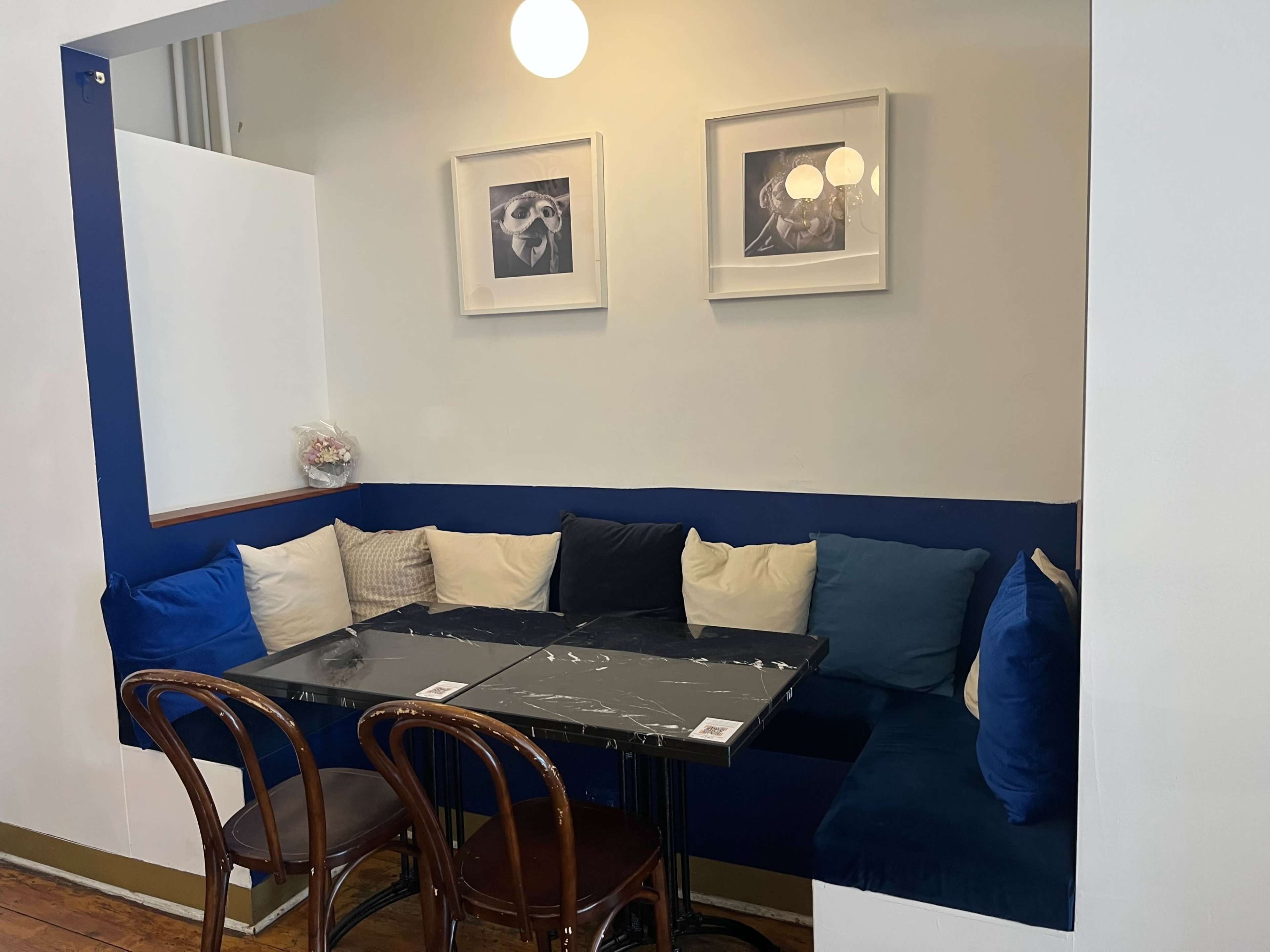 A cozy corner seating area features a dark table surrounded by a blue and white cushion-lined bench, with framed pictures on the wall above.