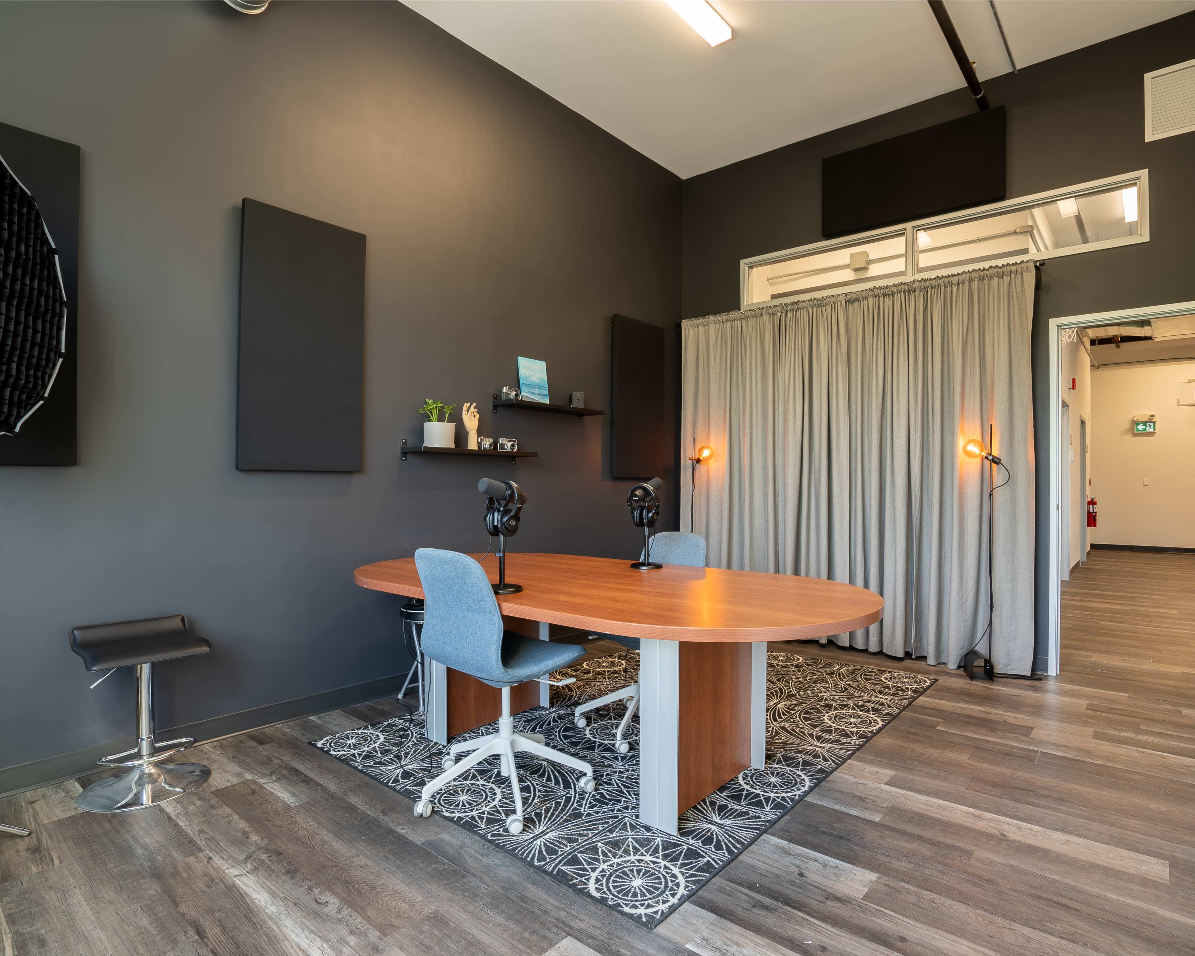 A modern workspace with a round wooden table, two chairs, a large rug, and soundproof panels on the walls.