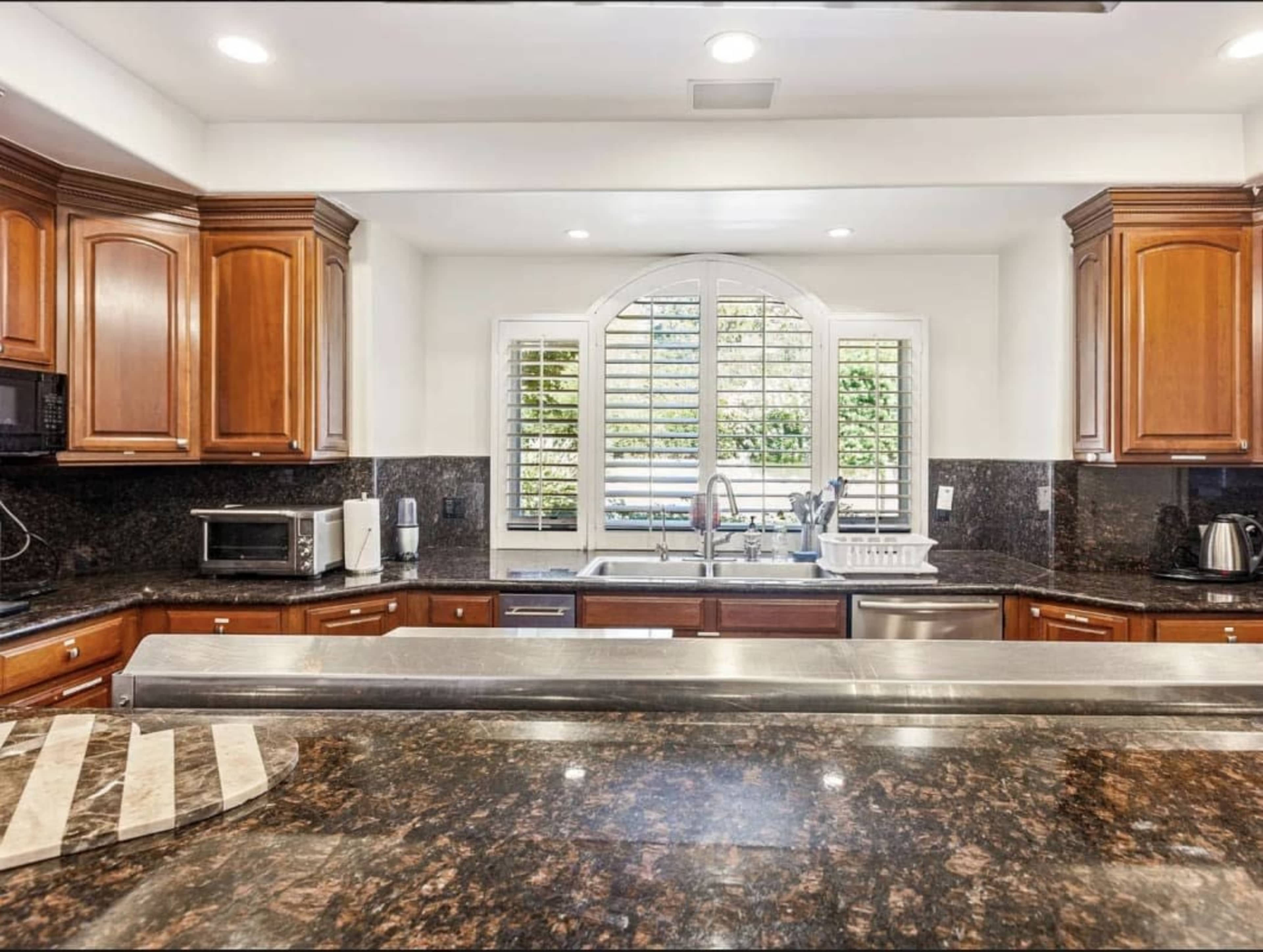 The image shows a modern kitchen with dark wood cabinetry, granite countertops, and a large window with plantation shutters above the sink.