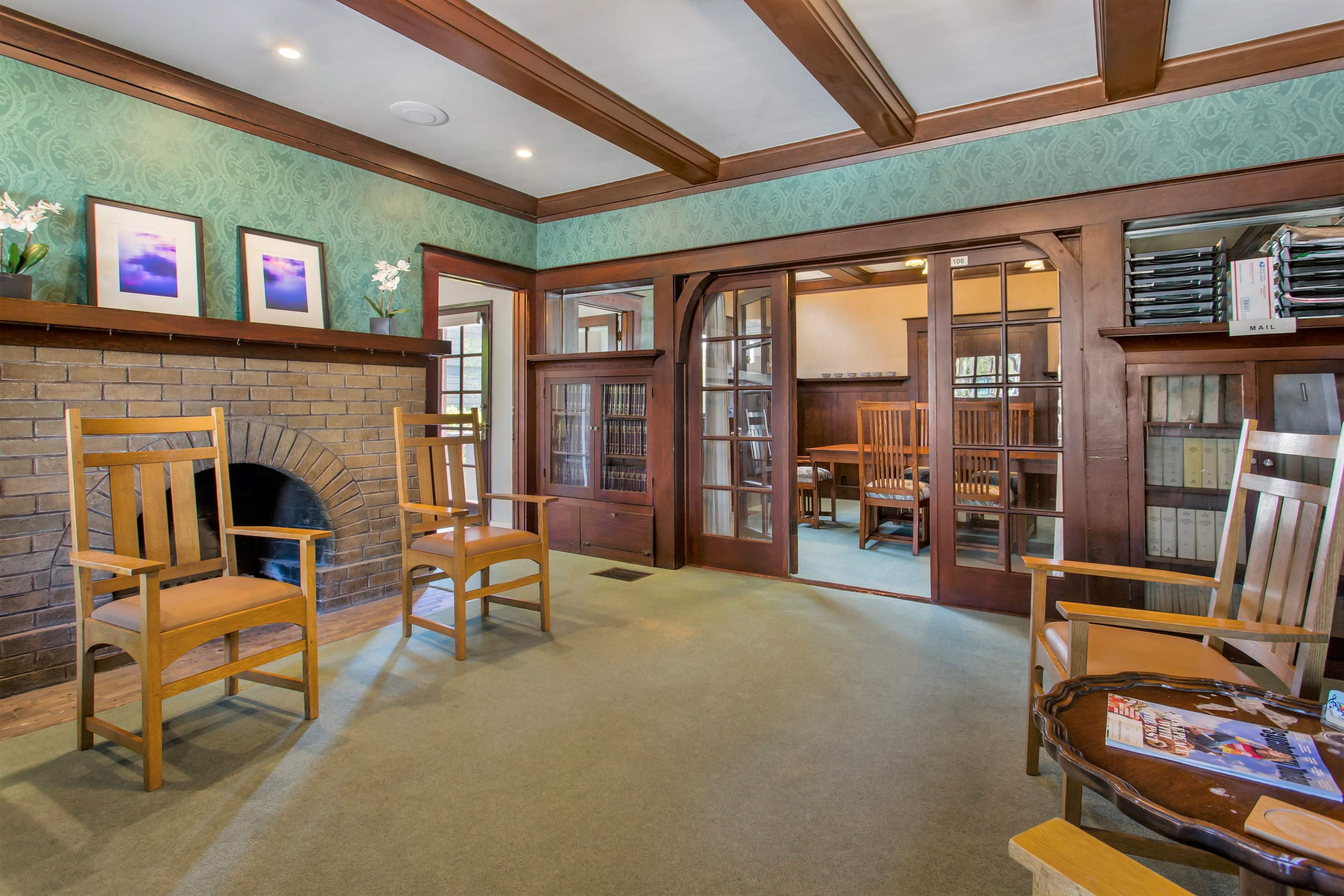 A room with wooden chairs arranged near a fireplace, featuring green wallpaper and large double doors leading to another space.