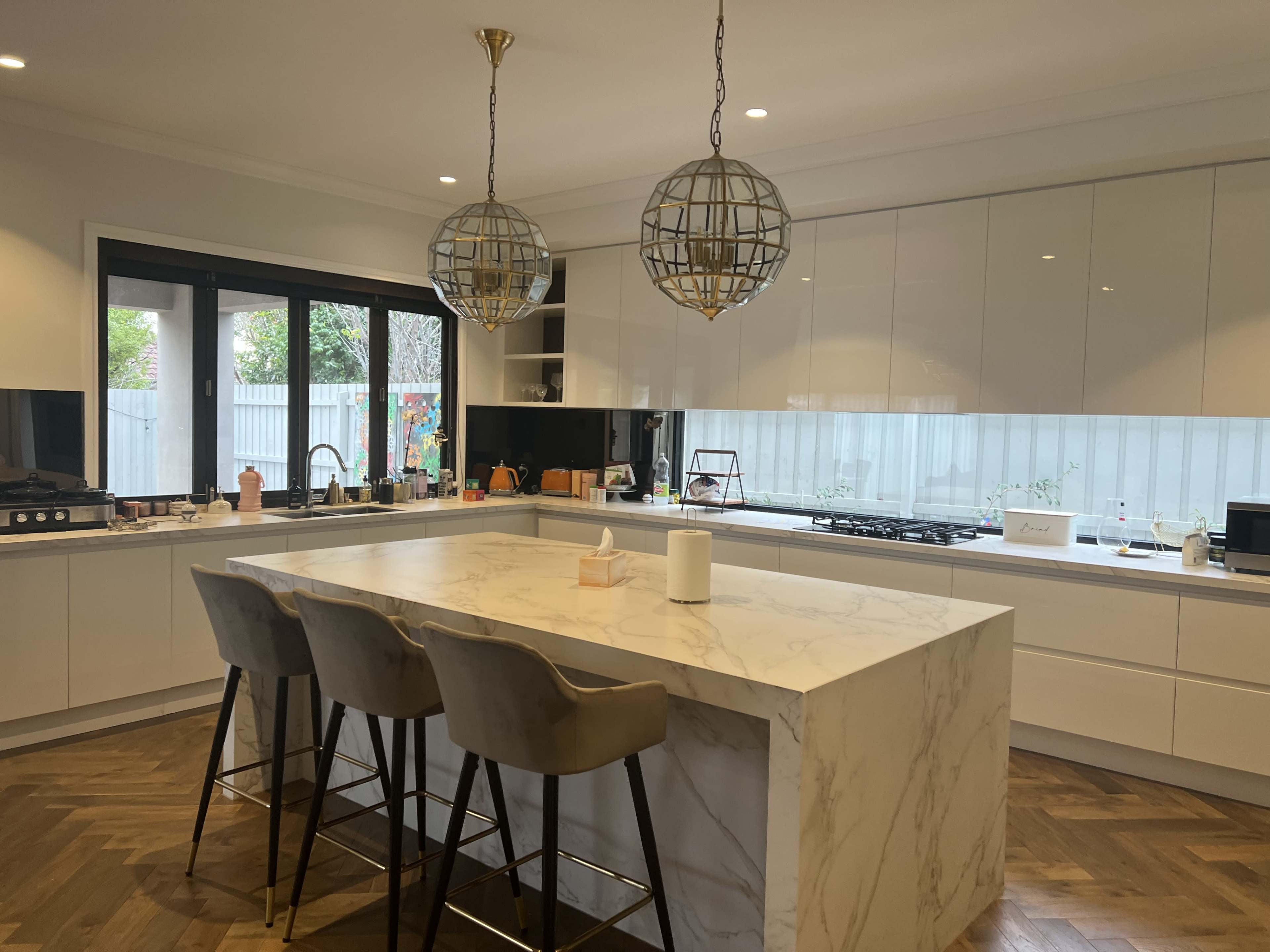 A modern kitchen with a large marble island, three bar stools, and two decorative pendant lights hanging from the ceiling.