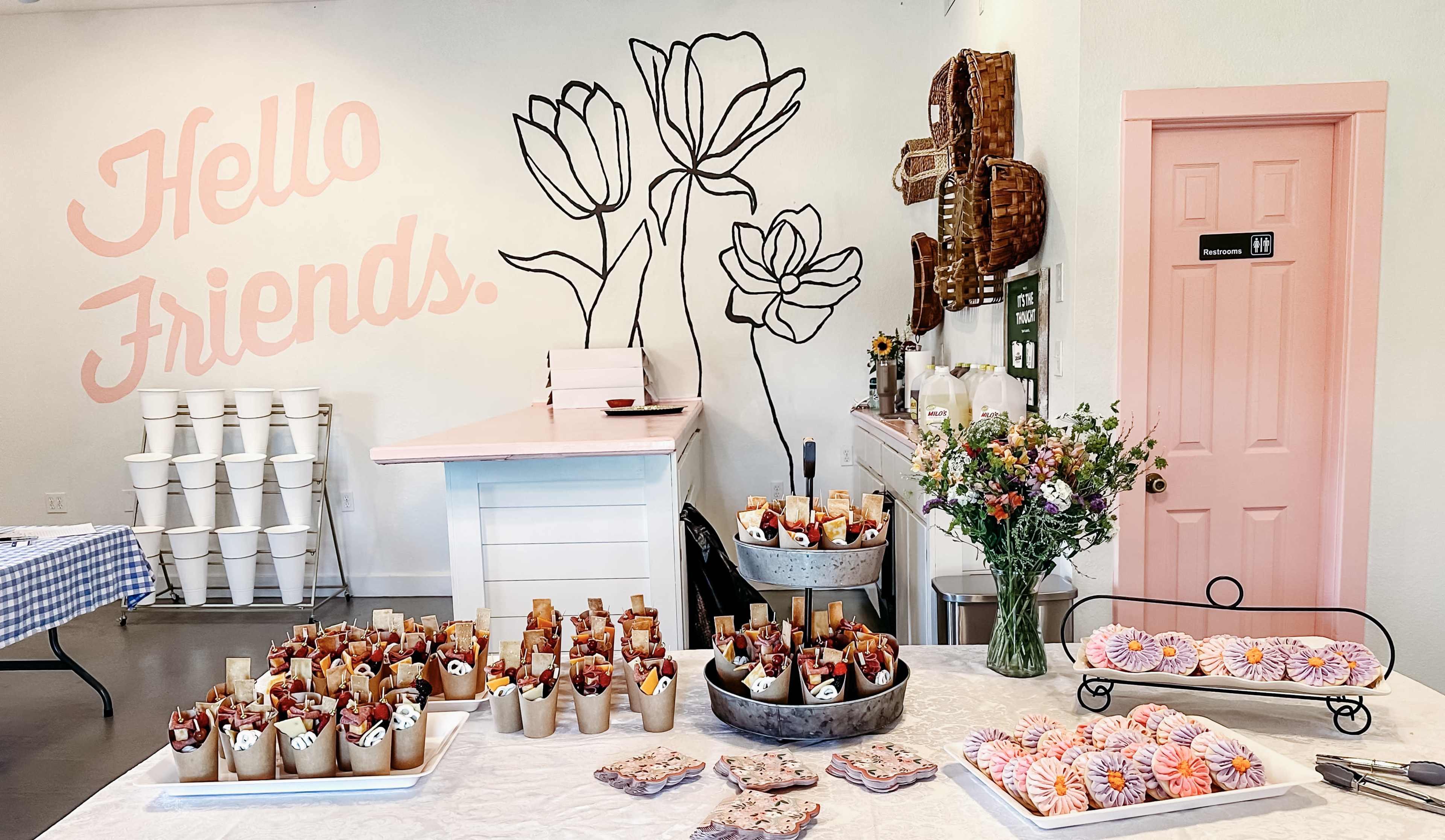 A brightly lit interior features a decorated counter with an array of desserts and a large floral mural on the wall.