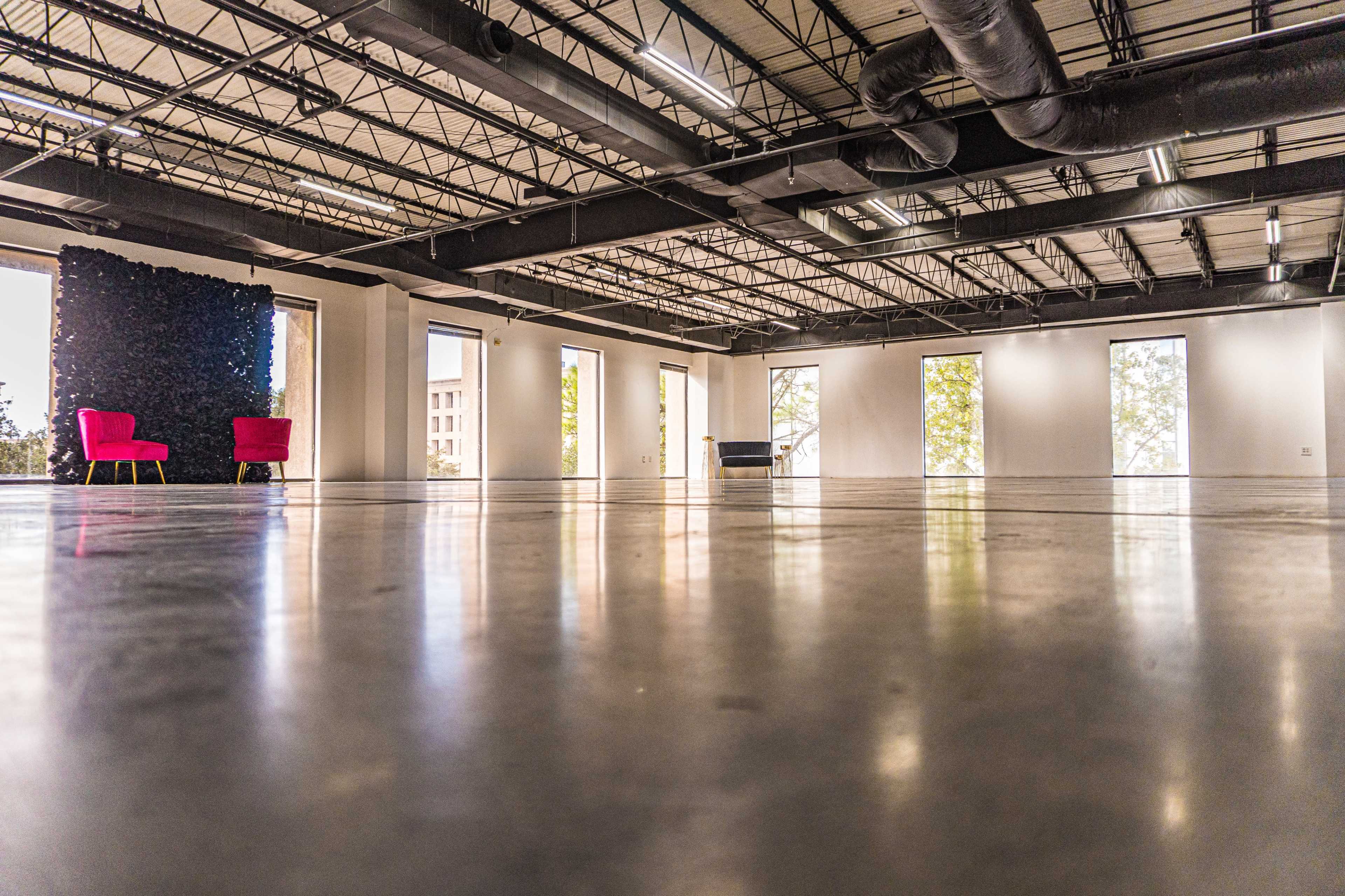 An empty modern space features polished concrete floors, large windows, and a pair of red chairs against a green wall.