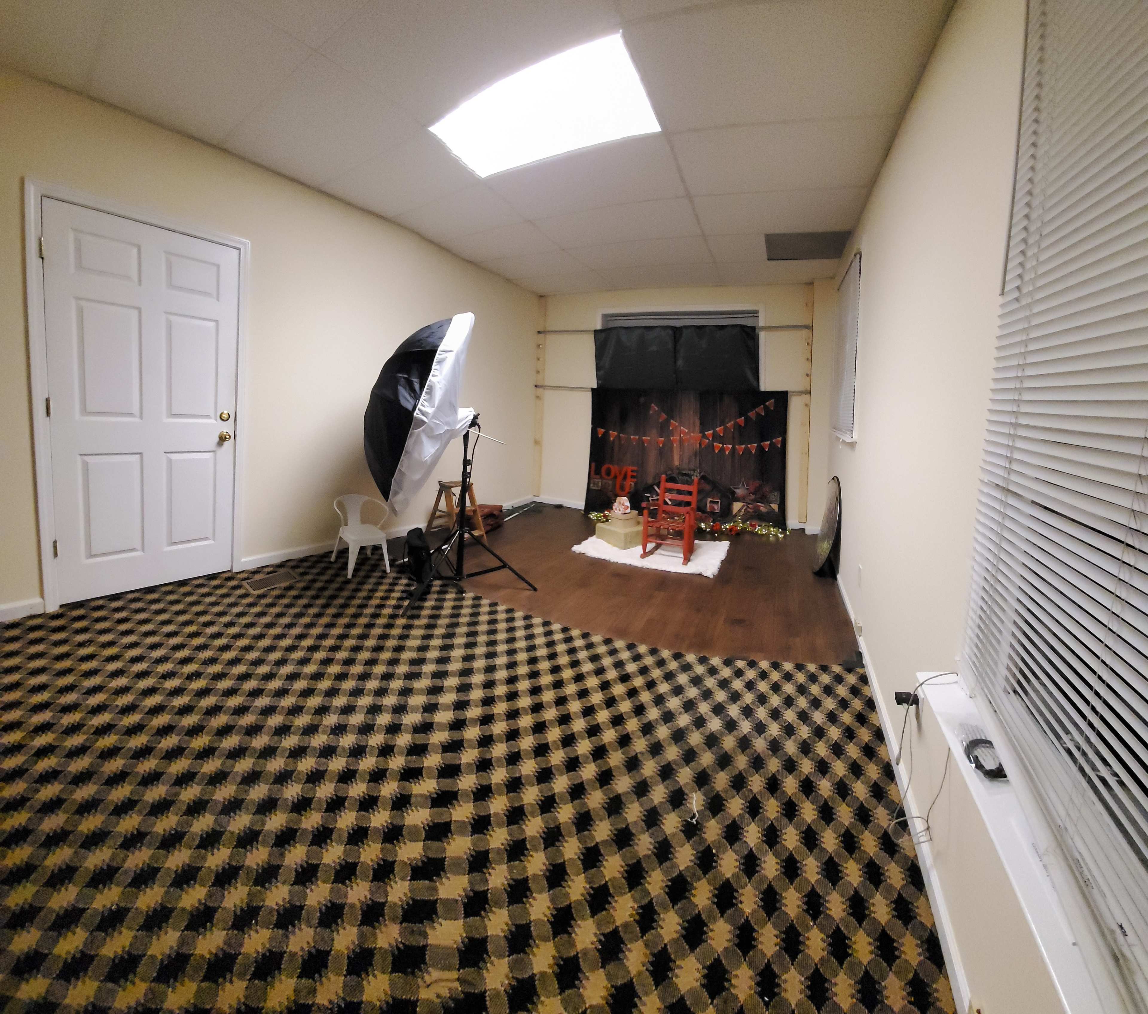 An empty studio space with a checkered floor, a backdrop with decorations, a chair, and photography equipment set up for a shoot.