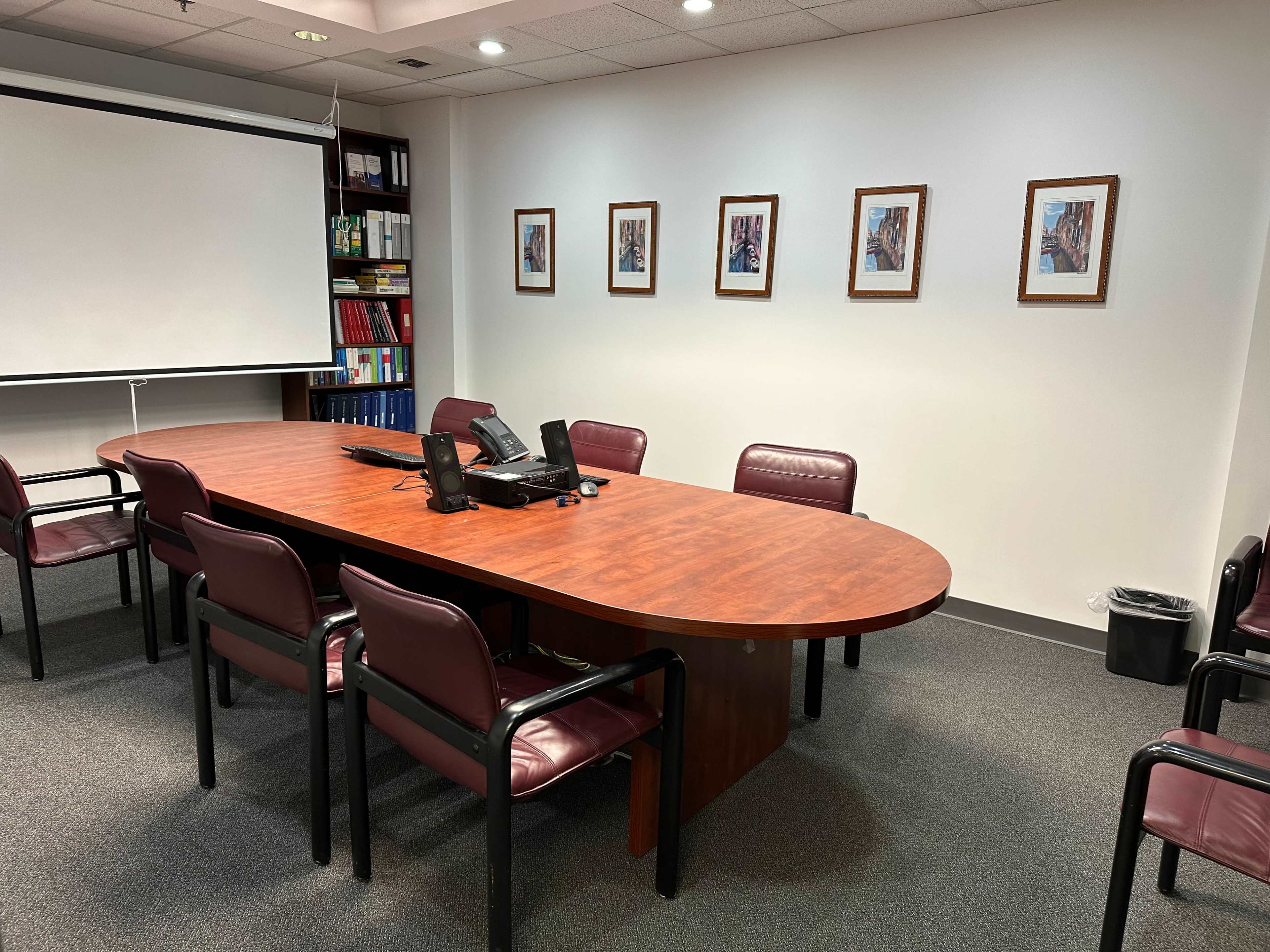 The image shows a conference room with a large oval table surrounded by chairs, a telephone on the table, and framed pictures on the walls.