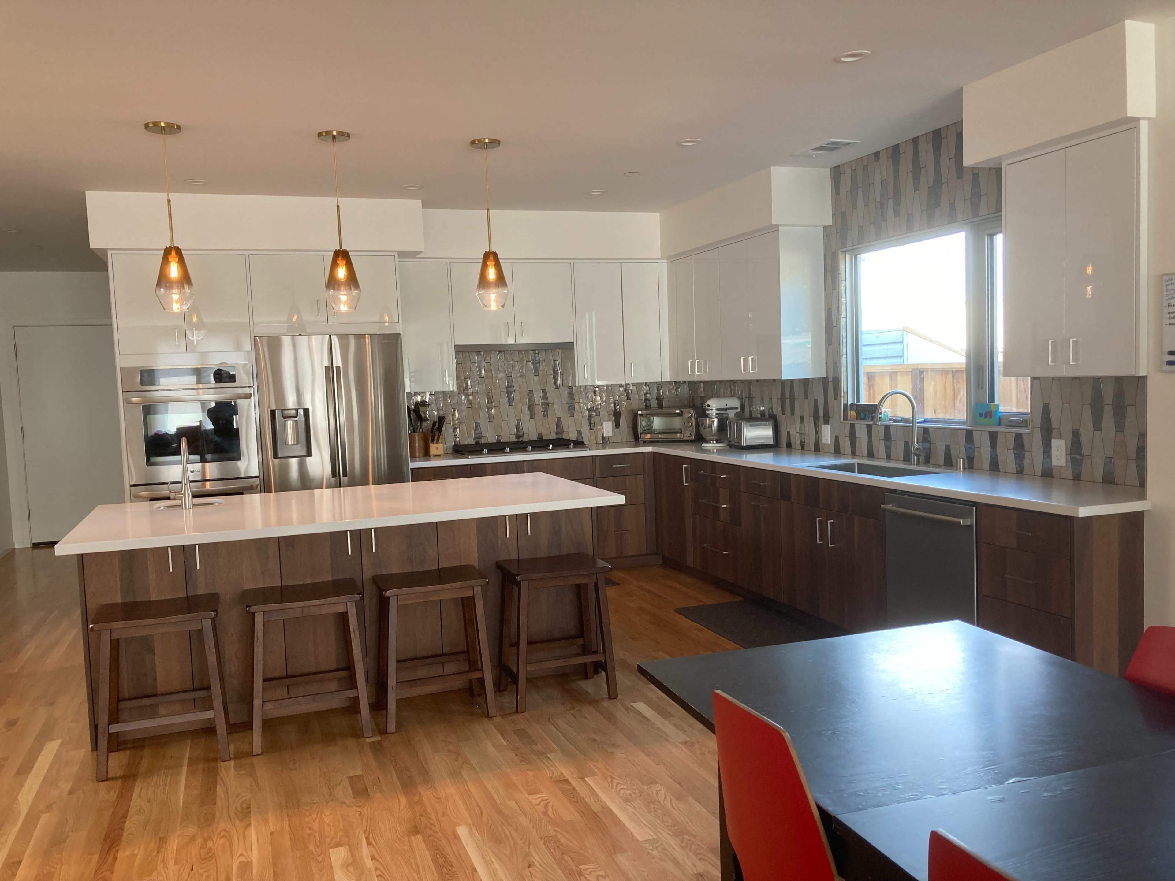 The kitchen features a large island with bar stools, modern cabinetry, and stainless steel appliances against a backdrop of tiled walls and large windows.