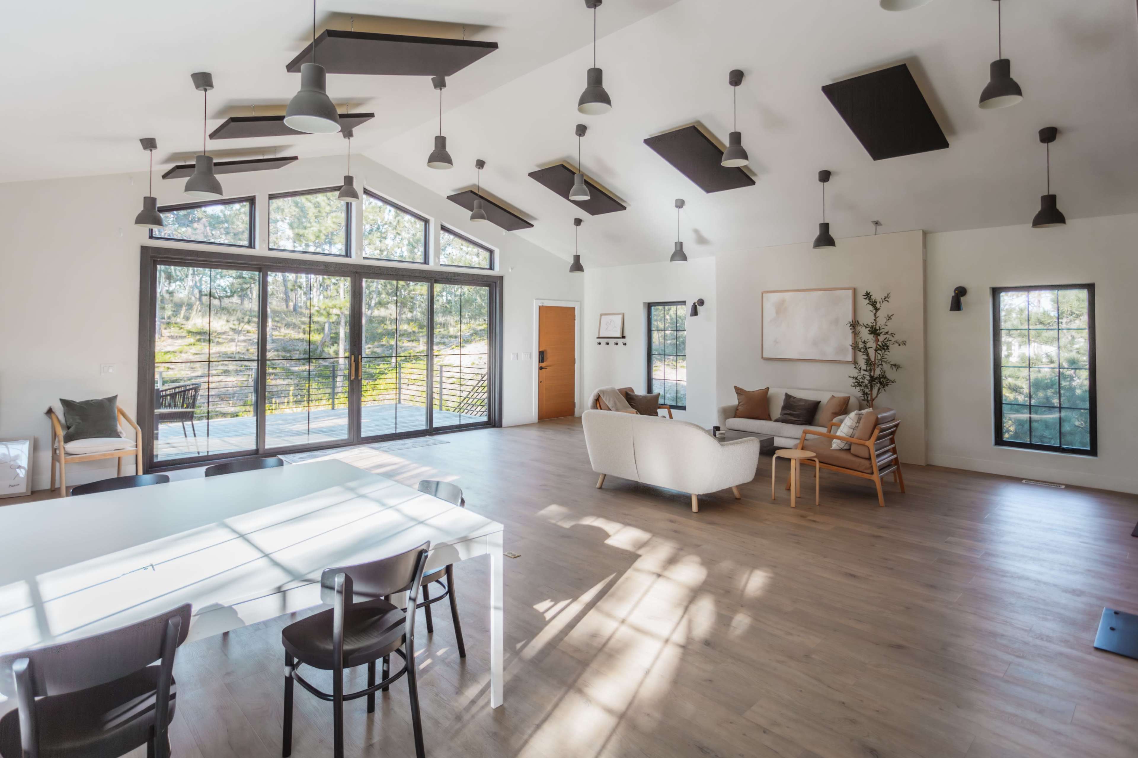 A spacious living area features large windows, a dining table, and various seating arrangements under pendant lights.