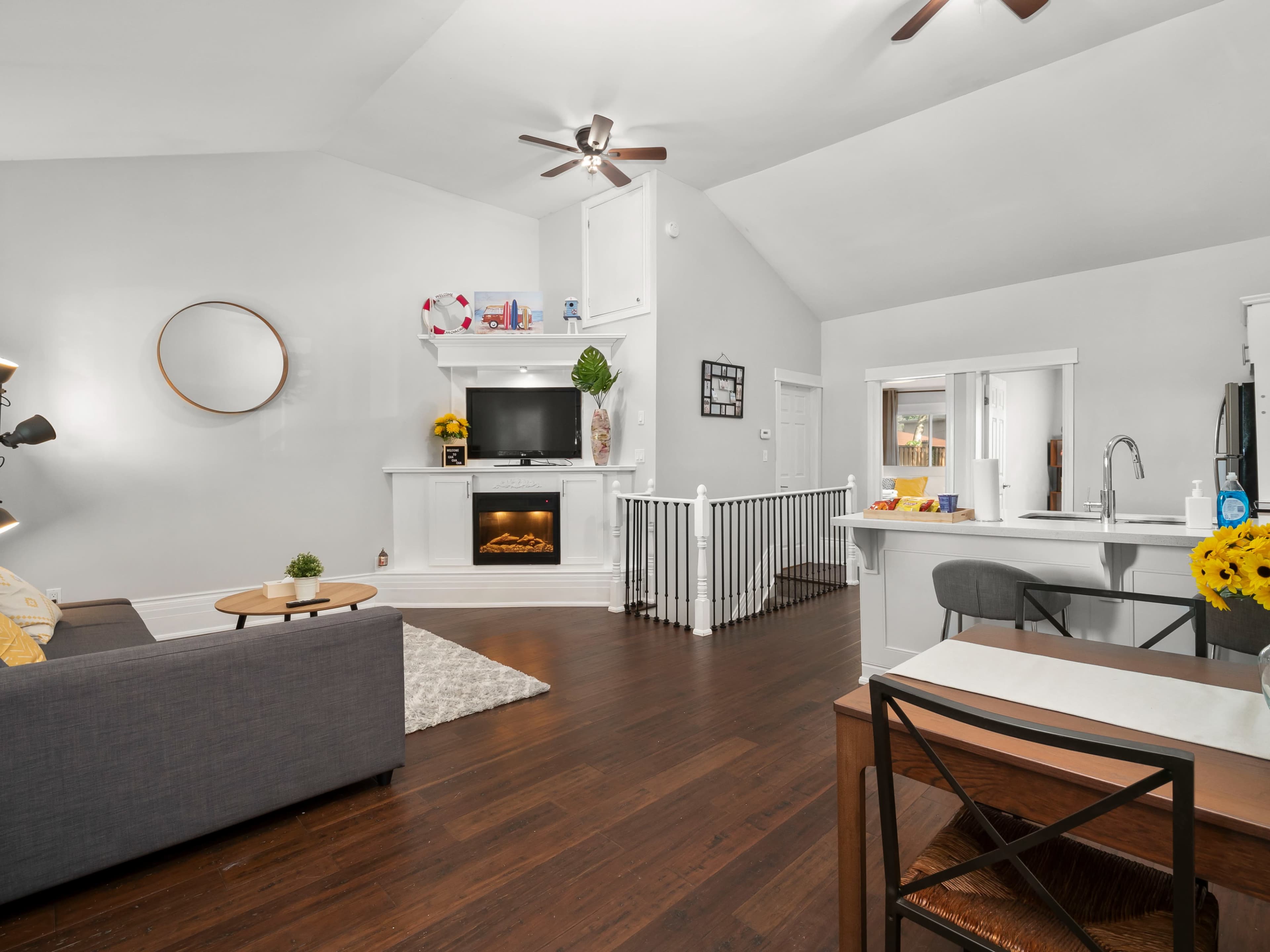 The living area features a gray sofa, a fireplace with a TV above it, and a dining space with a table near the kitchen.