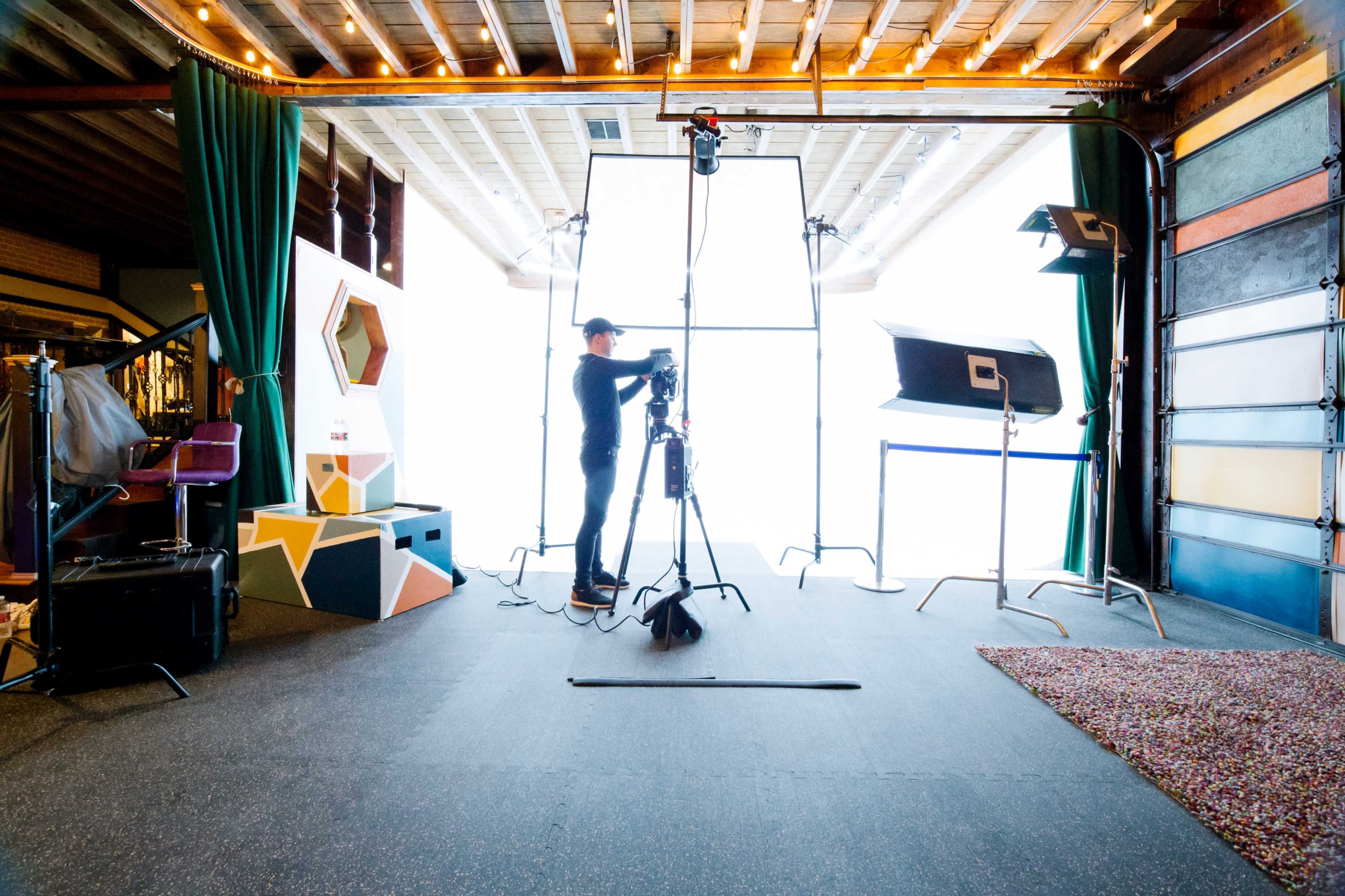 A photographer is adjusting equipment in a well-lit studio space featuring softboxes and a backdrop.
