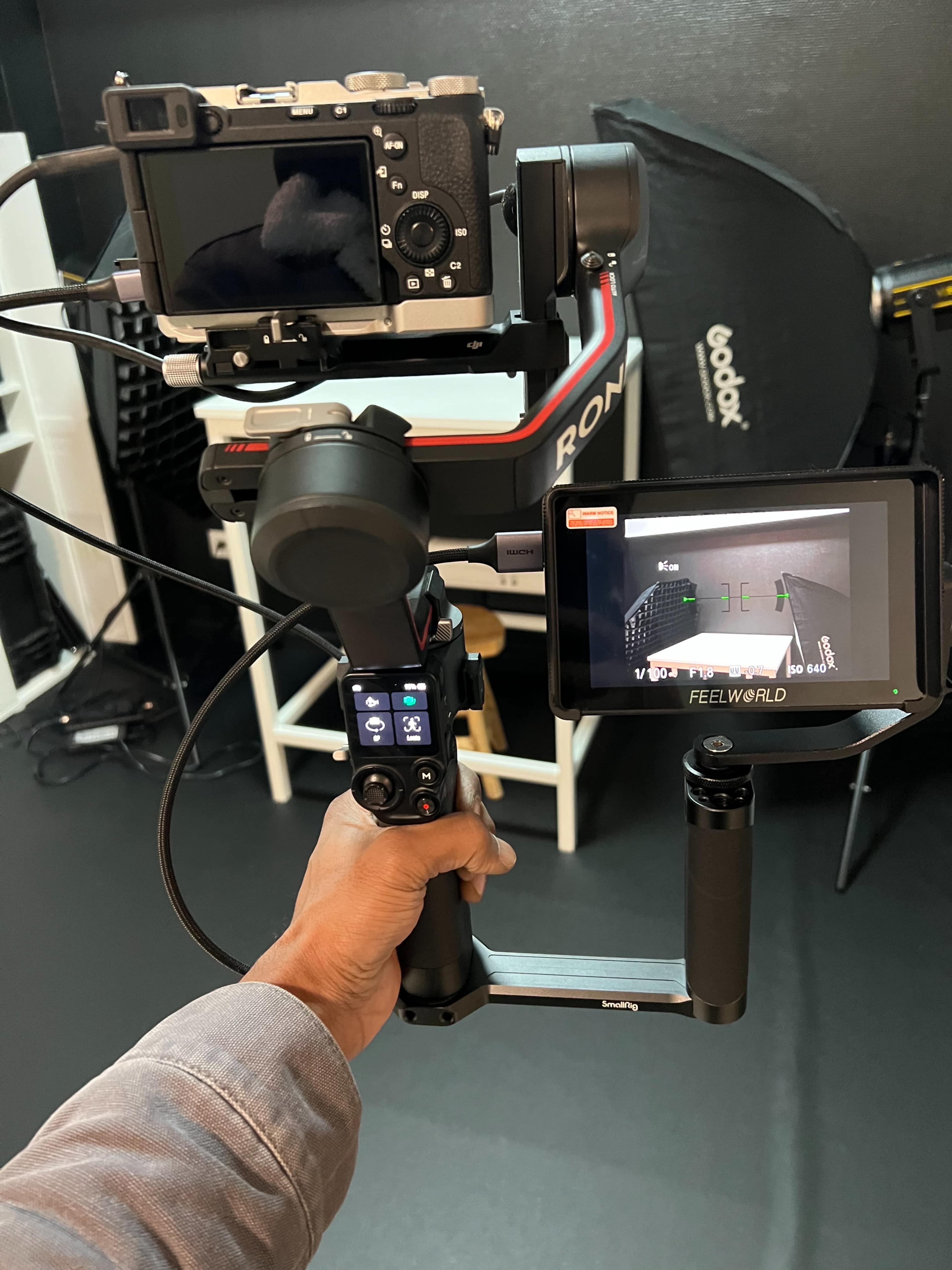 A person holds a camera mounted on a gimbal stabilizer with a monitor displaying a live feed attached.
