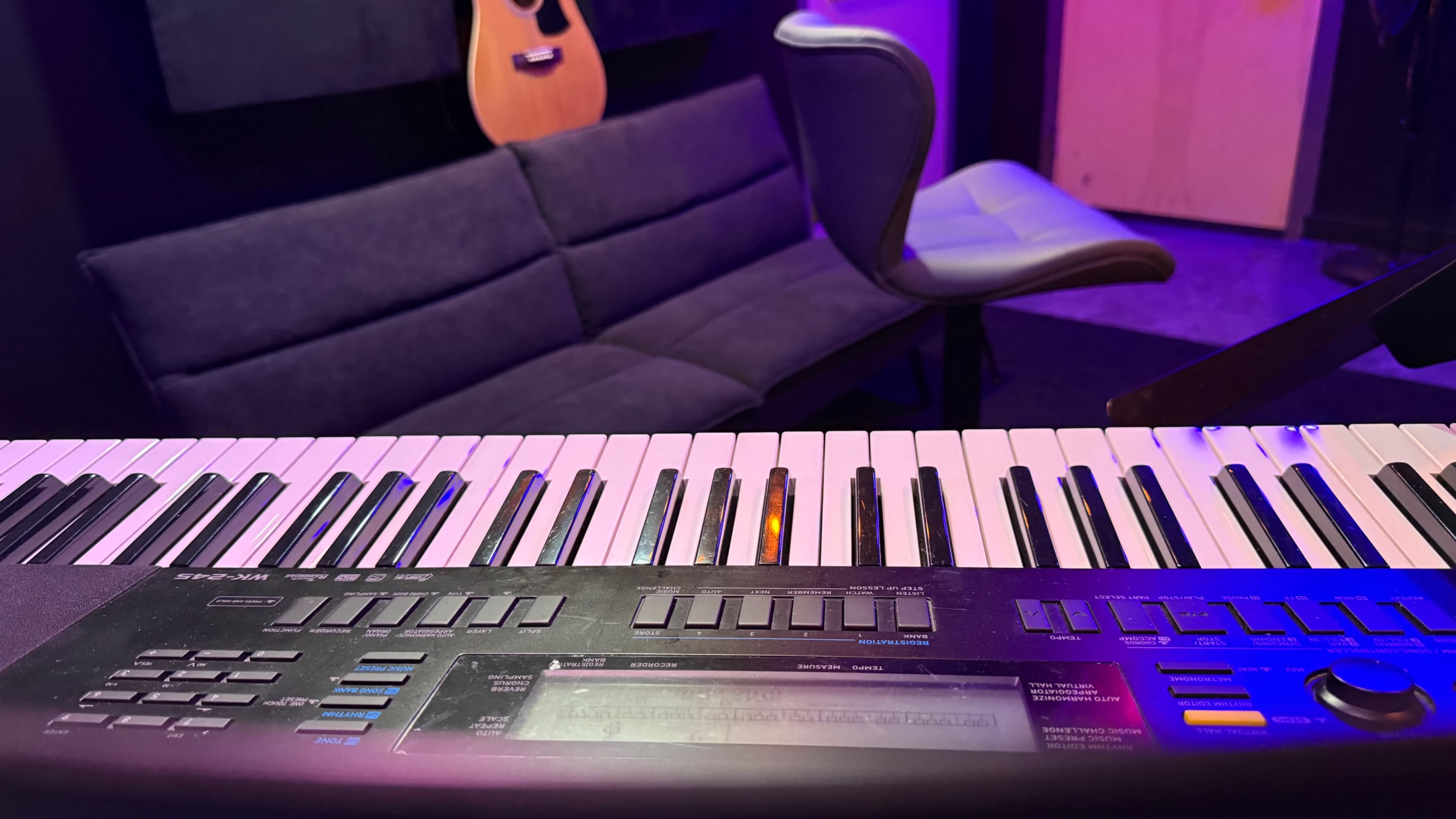 A keyboard is in the foreground with a sofa and a chair visible in the background of a dimly lit room.