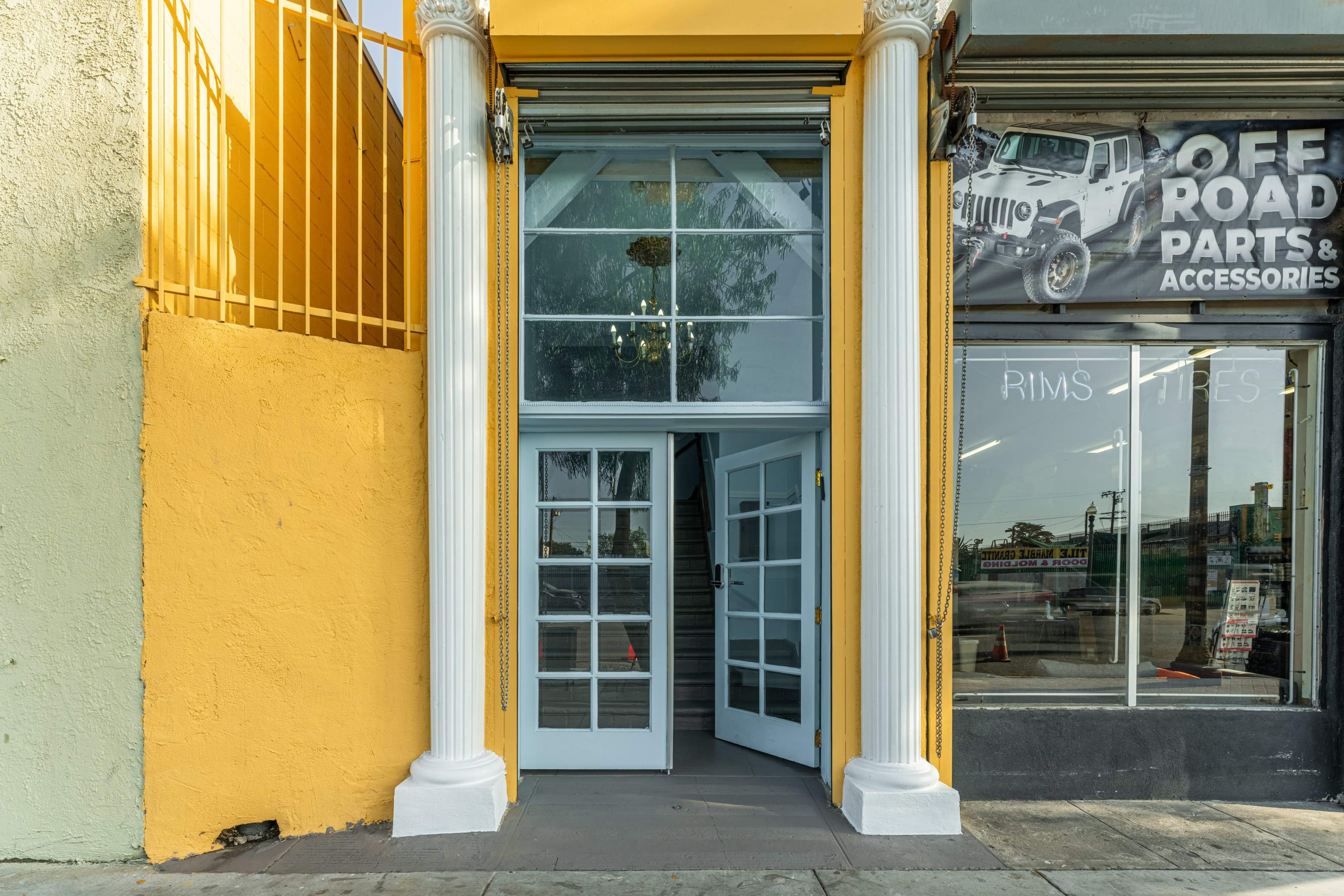 A storefront with a bright yellow exterior, featuring white columns flanking a glass double door entrance.