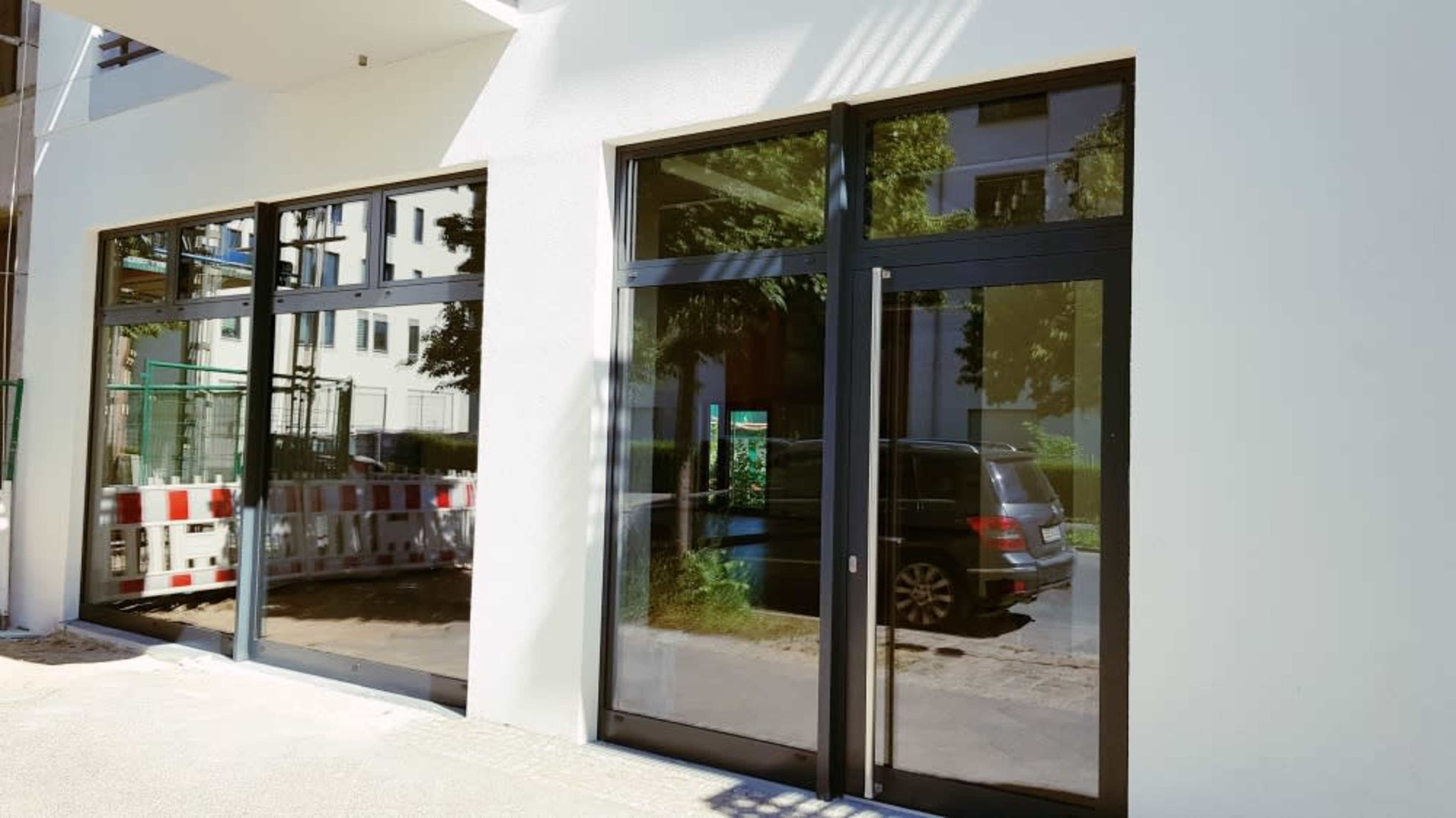 A building exterior with large glass windows and double doors, reflecting the surrounding area and displaying a parked car nearby.