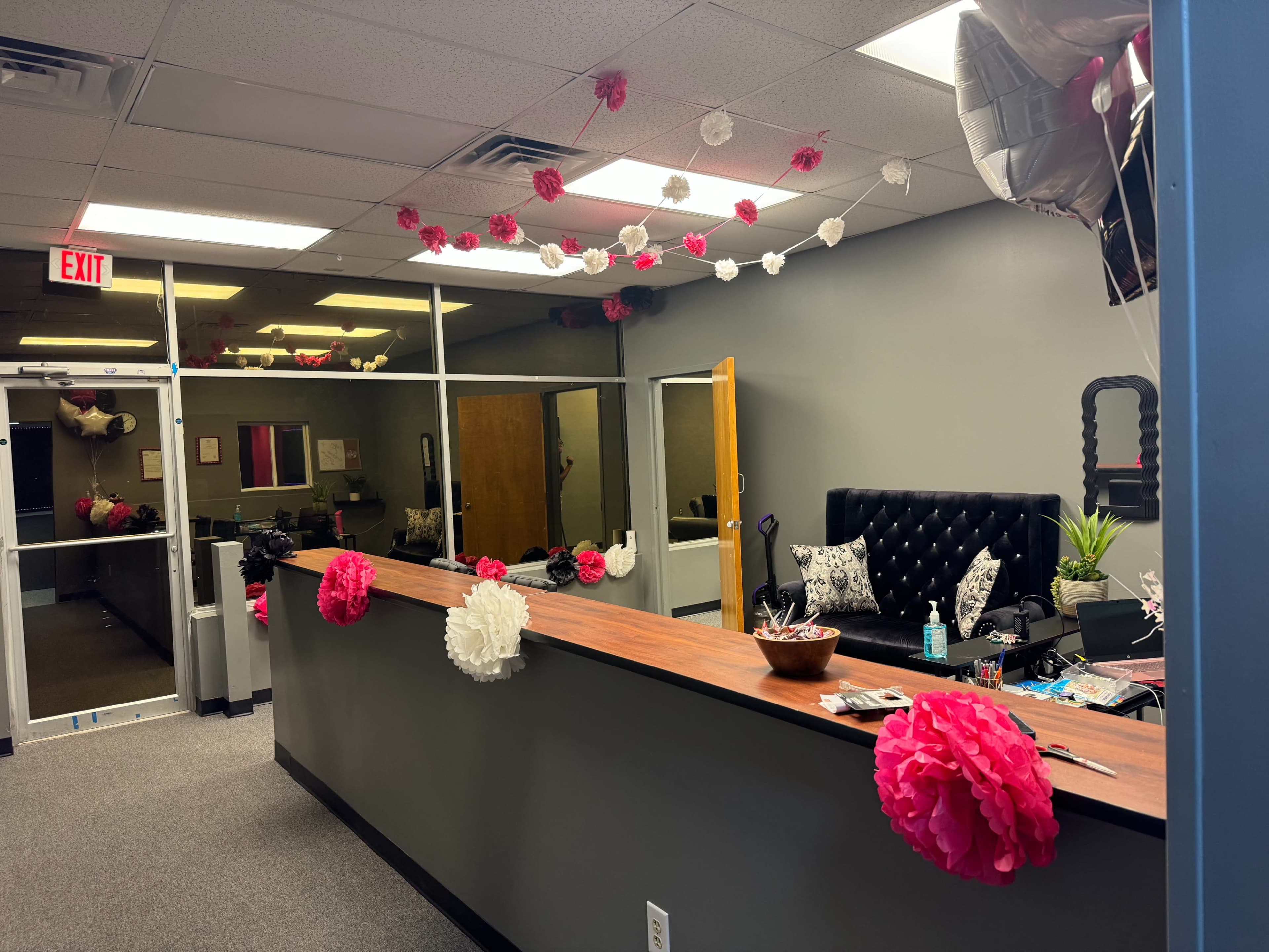 A reception area decorated with pink and white paper pom poms, featuring a dark upholstered chair and a wooden front desk.