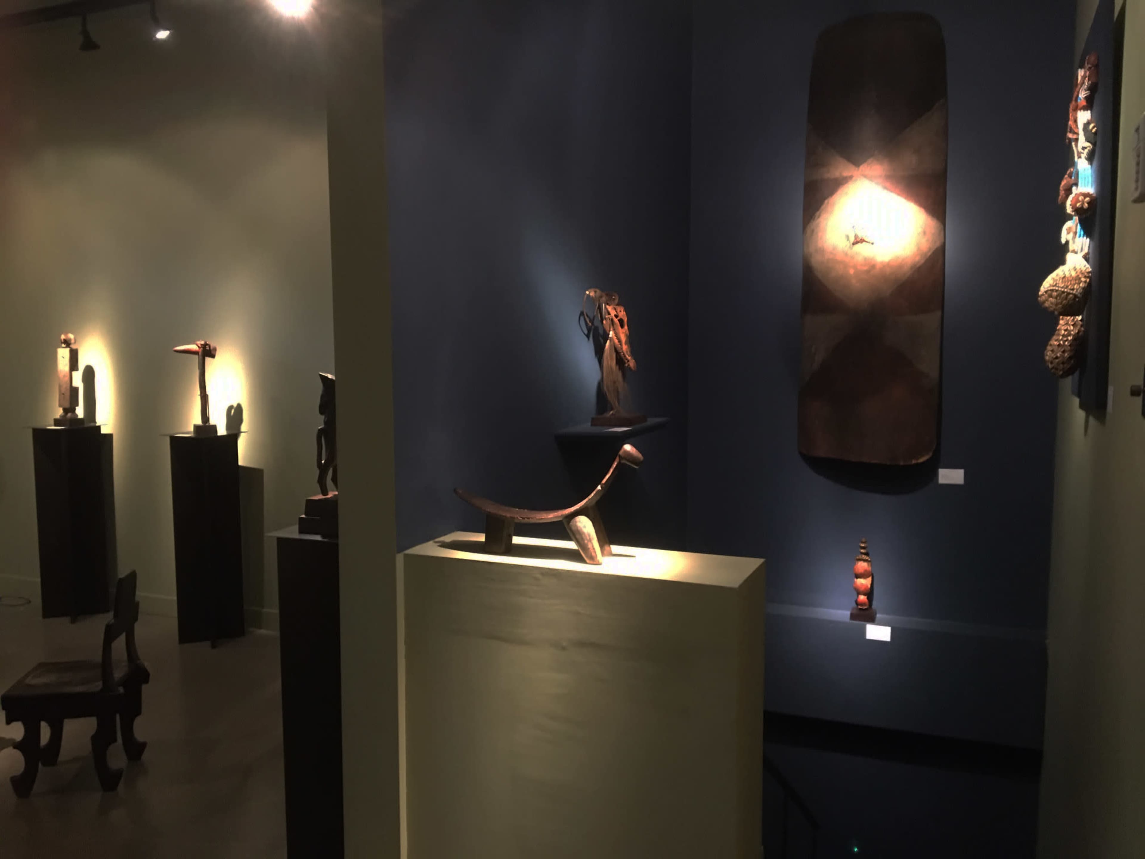 An art gallery exhibiting various sculptures and artifacts illuminated by accent lighting against dark blue and green walls.