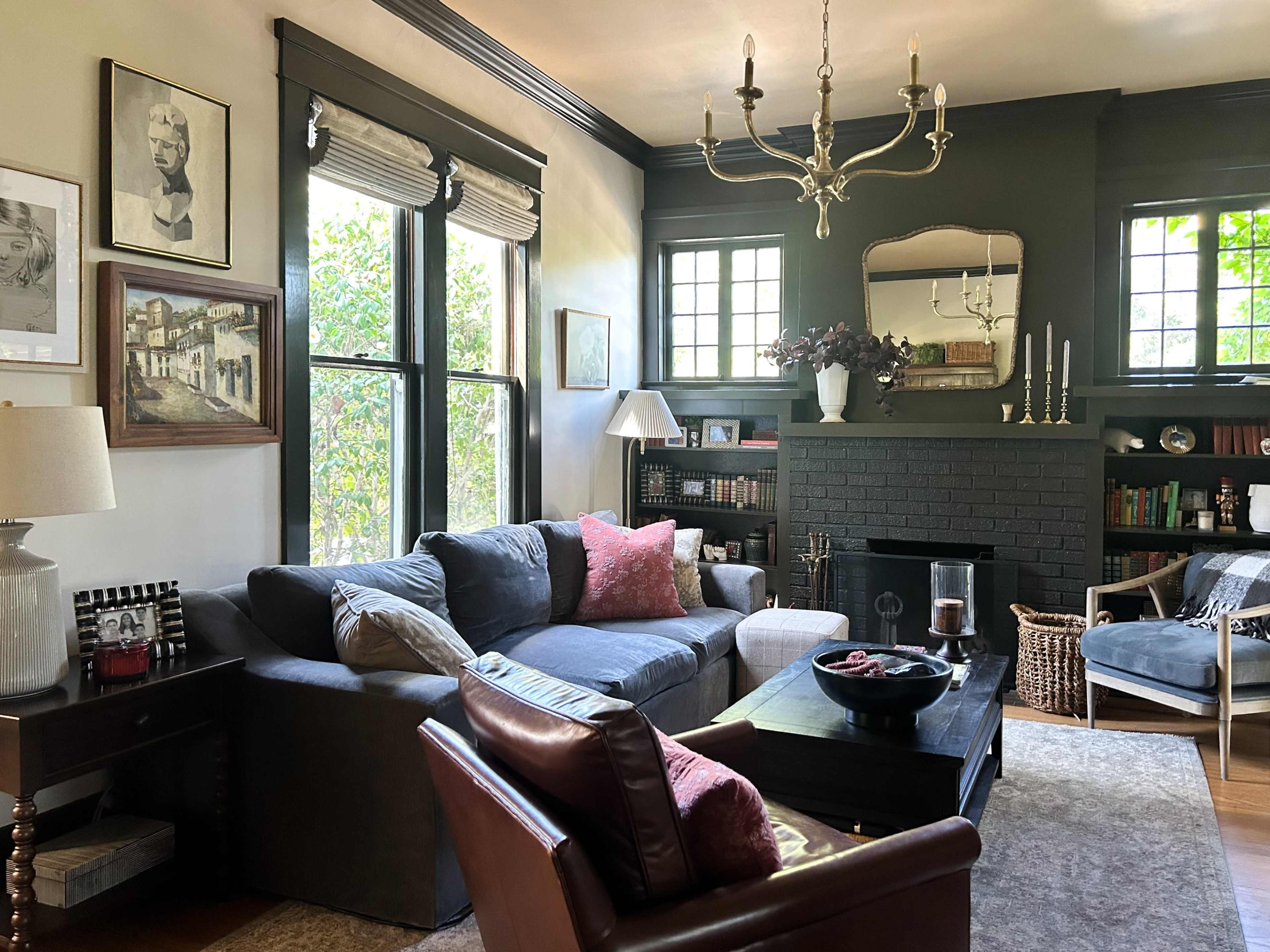 The living room features a gray sectional sofa and a dark fireplace, surrounded by large windows and framed artwork on the walls.