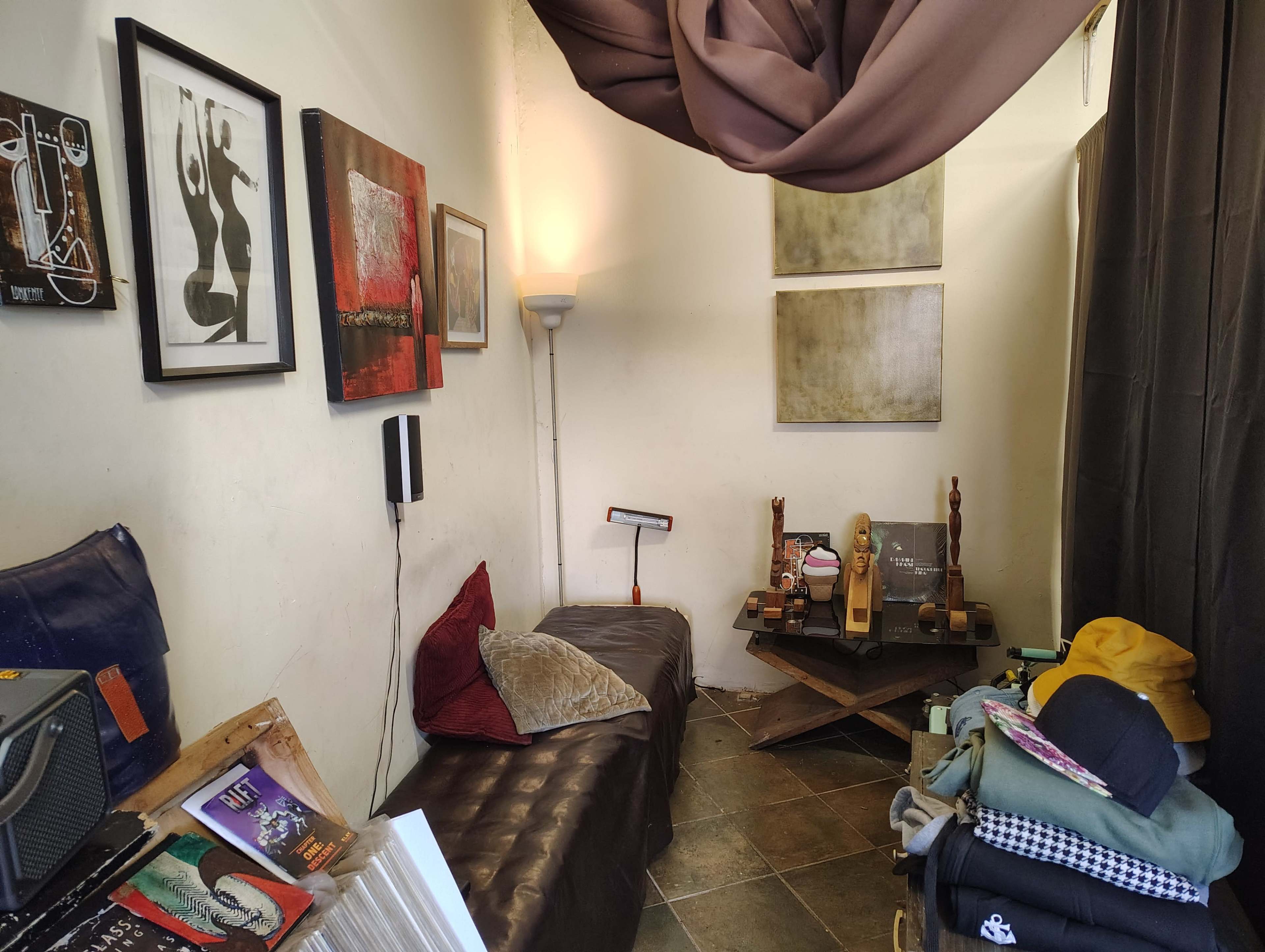 The image shows a small, cozy room with a dark sofa, artwork on the walls, and a lamp illuminating a corner with decorative items on a table.