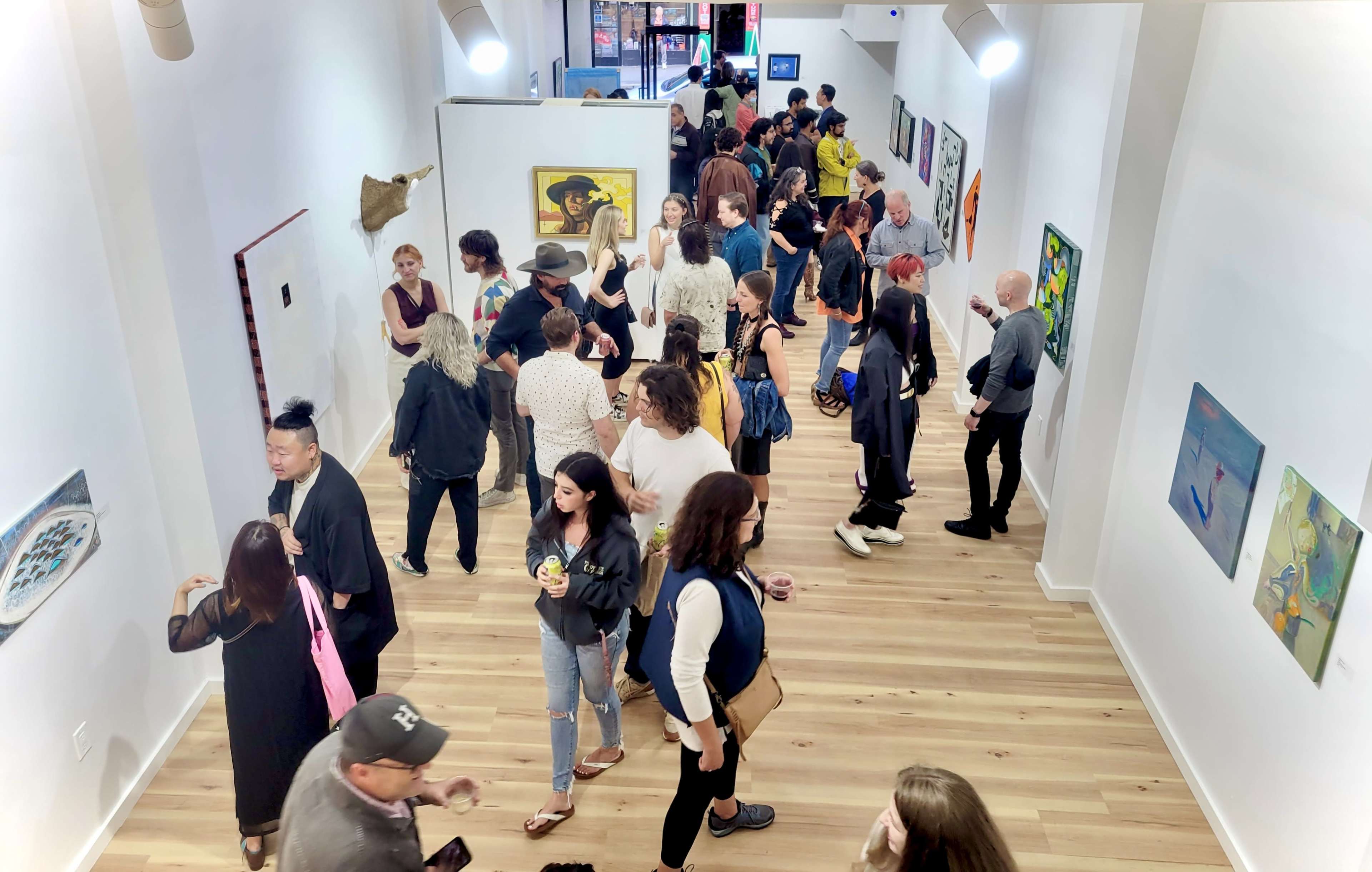 A crowded art gallery features visitors interacting with various artworks displayed on white walls.