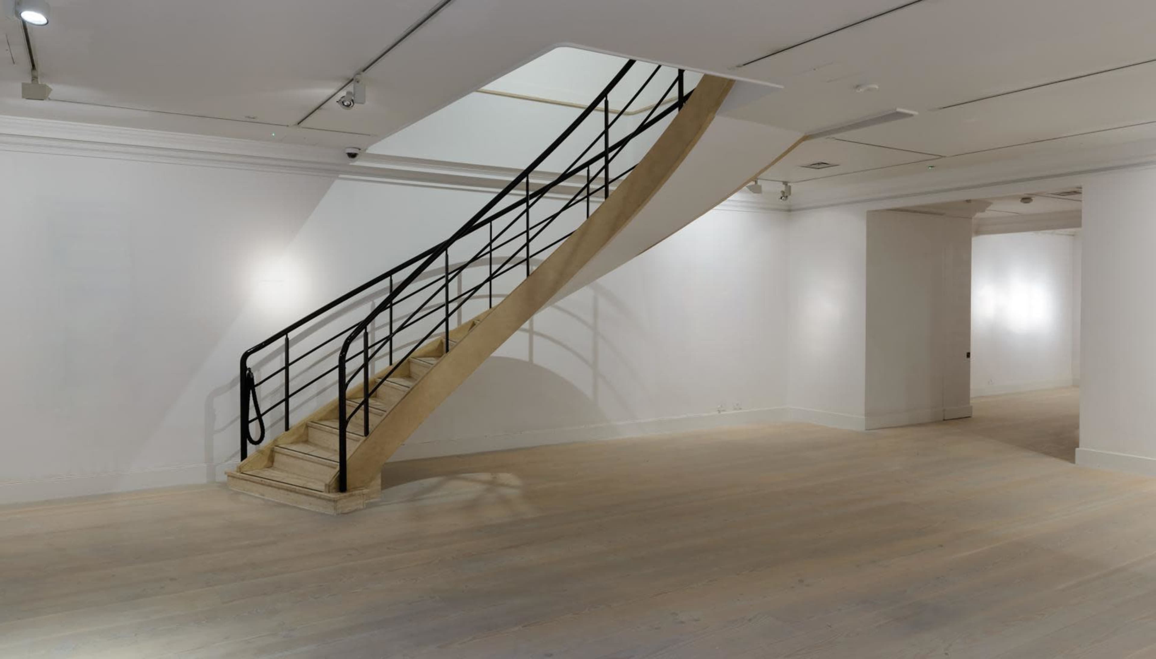 A minimalist interior space with a curved staircase leading to an upper level against a plain white wall.