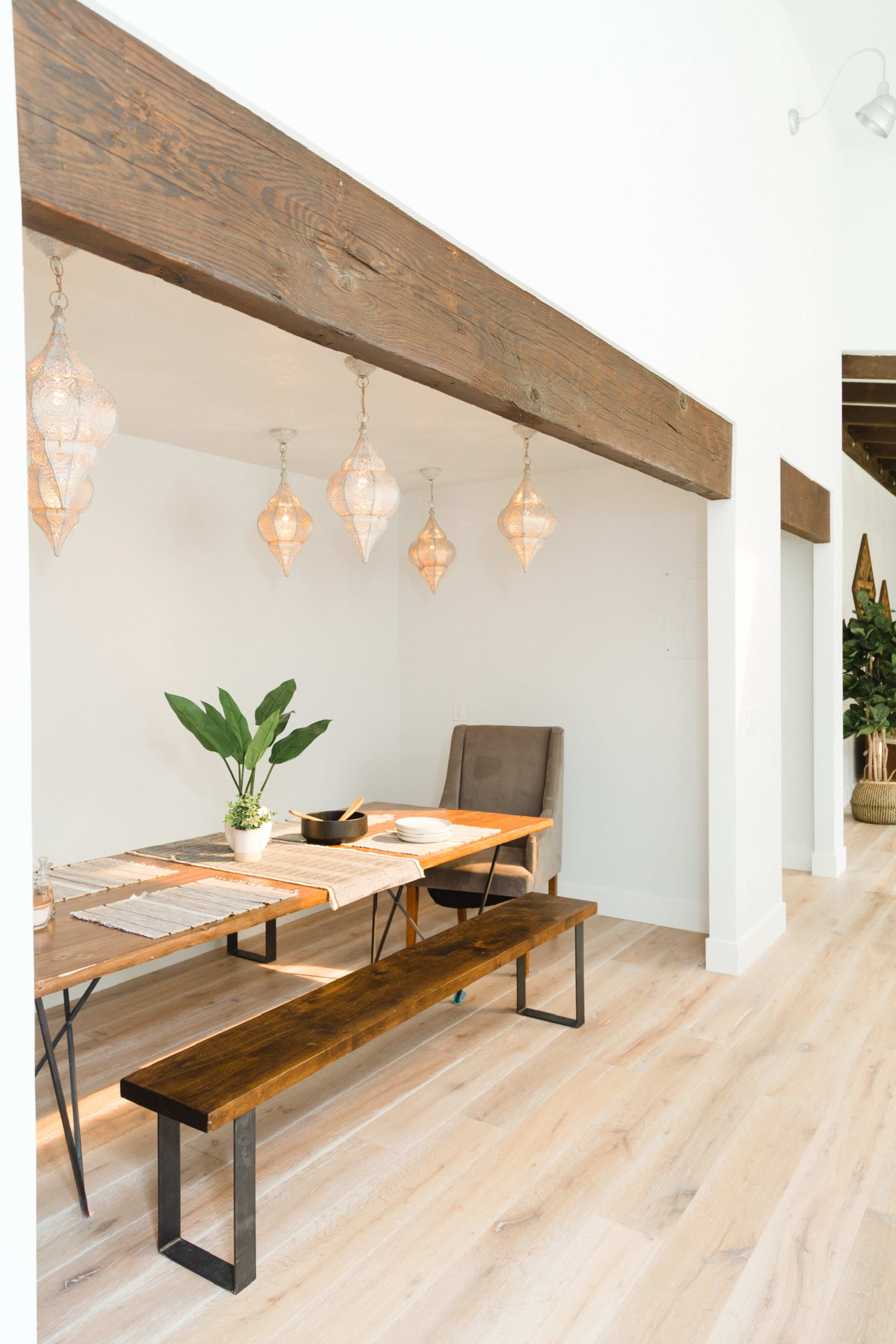 A dining area features a wooden table, a bench, and hanging pendant lights with a plant nearby.