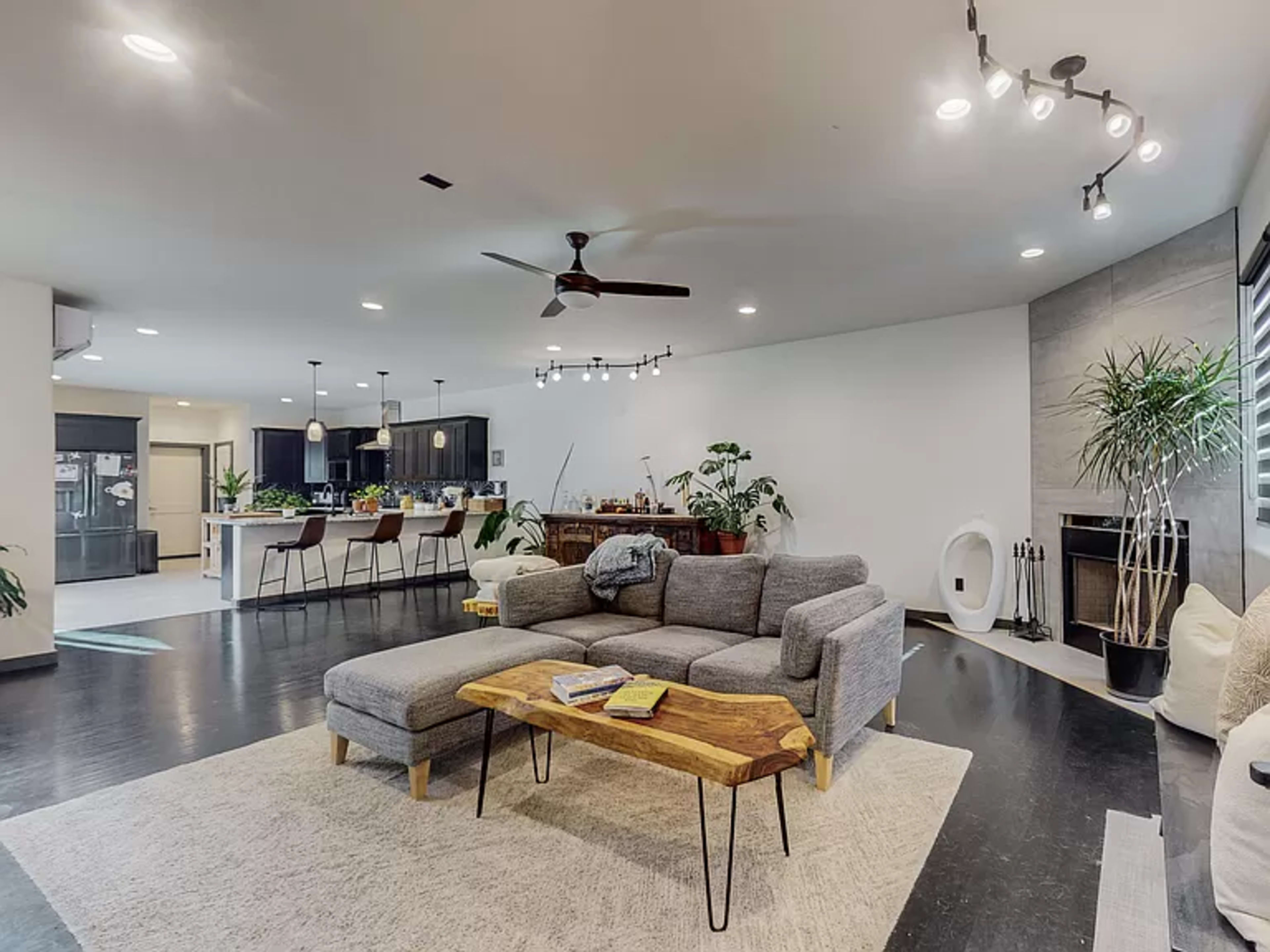 A modern living room with a gray sectional sofa, a wooden coffee table, and a view of a dining area with a kitchen in the background.