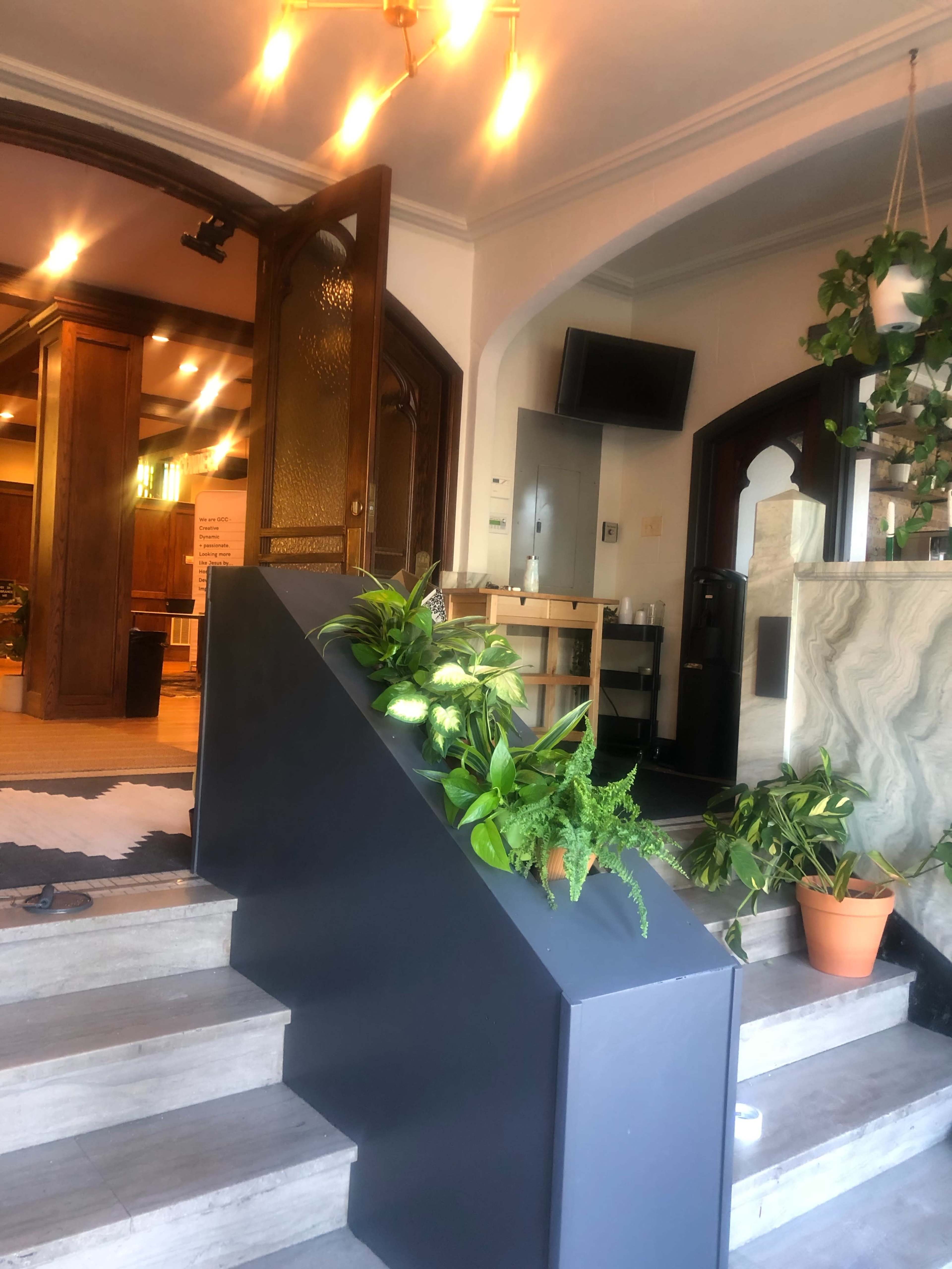 An indoor staircase with plants arranged along the side, leading to a well-lit reception area.