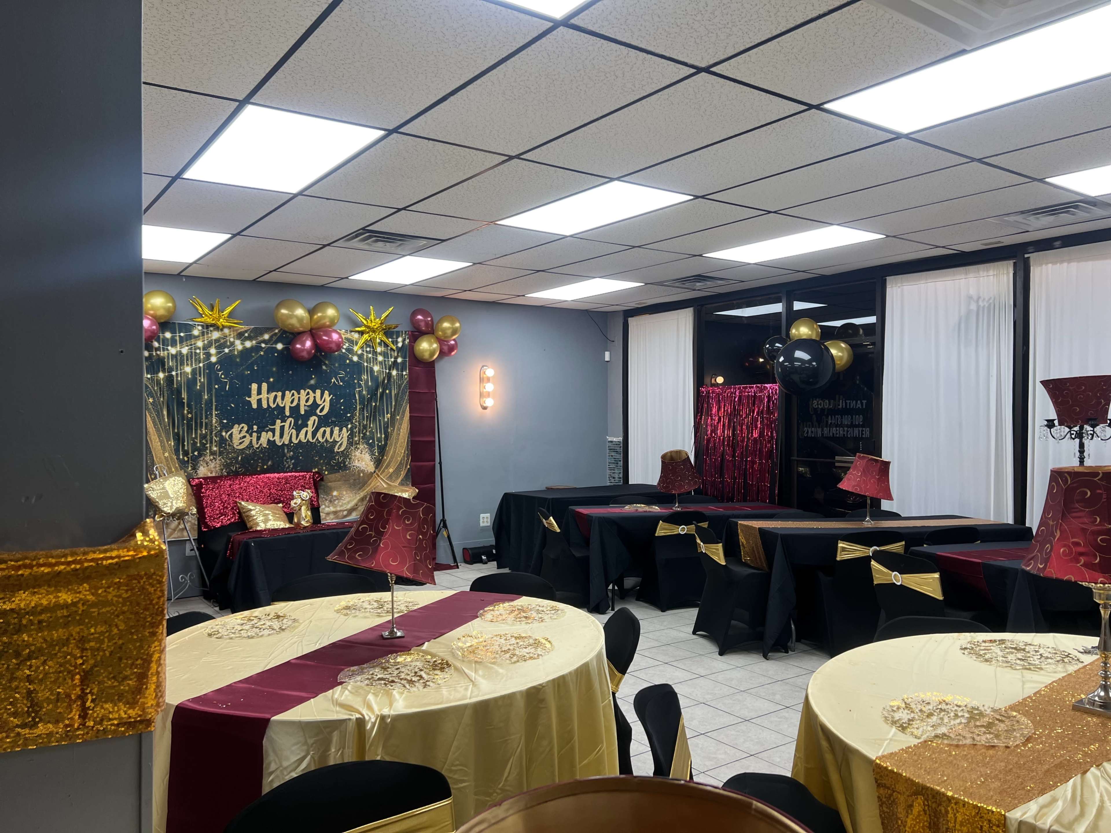 The image shows a decorated birthday party venue with tables covered in gold and black tablecloths, a backdrop that reads "Happy Birthday," and colorful balloons.