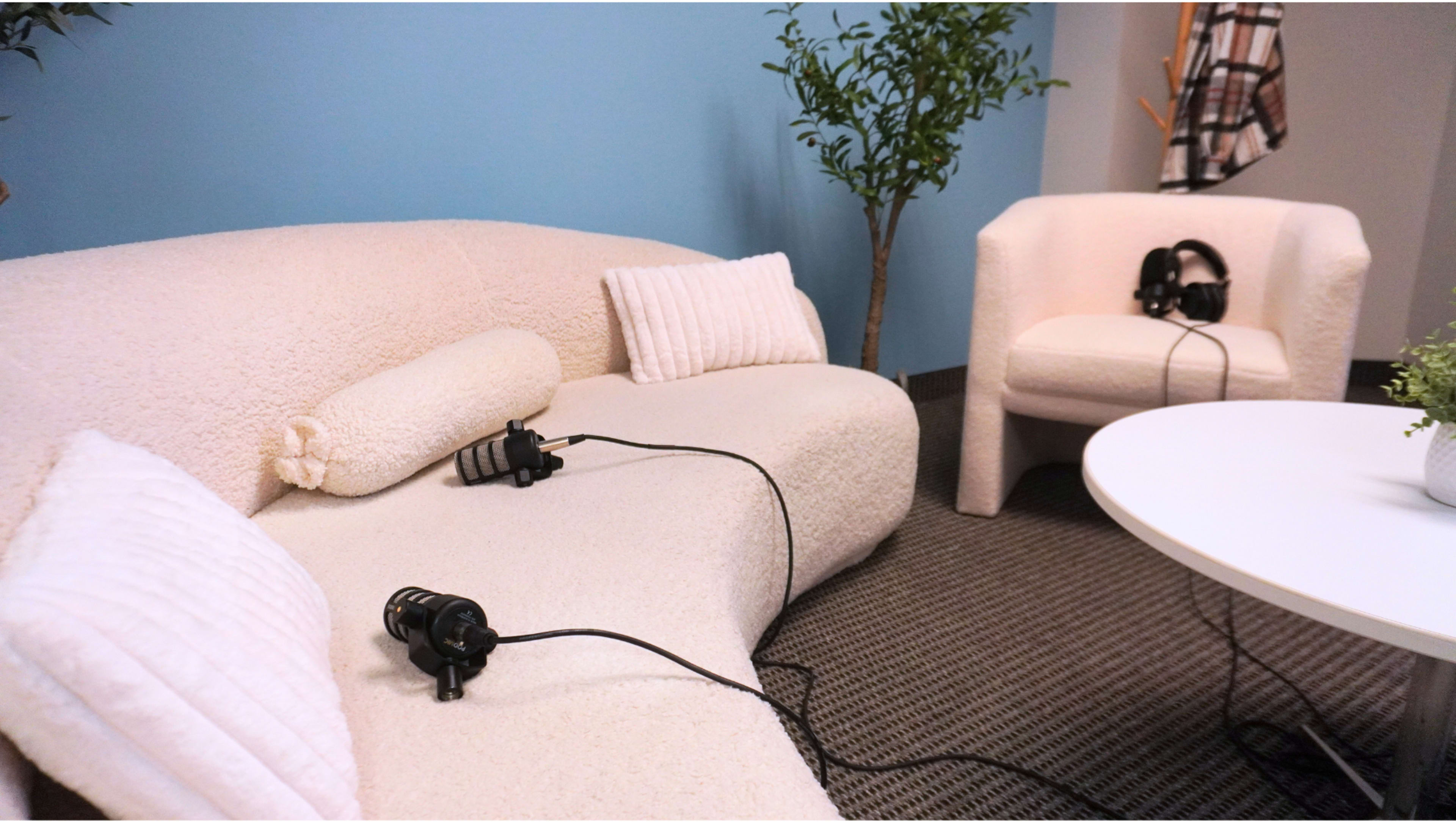A cozy seating area features a white, textured couch and chair with headphones resting on them, surrounded by a small table and decorative plants.