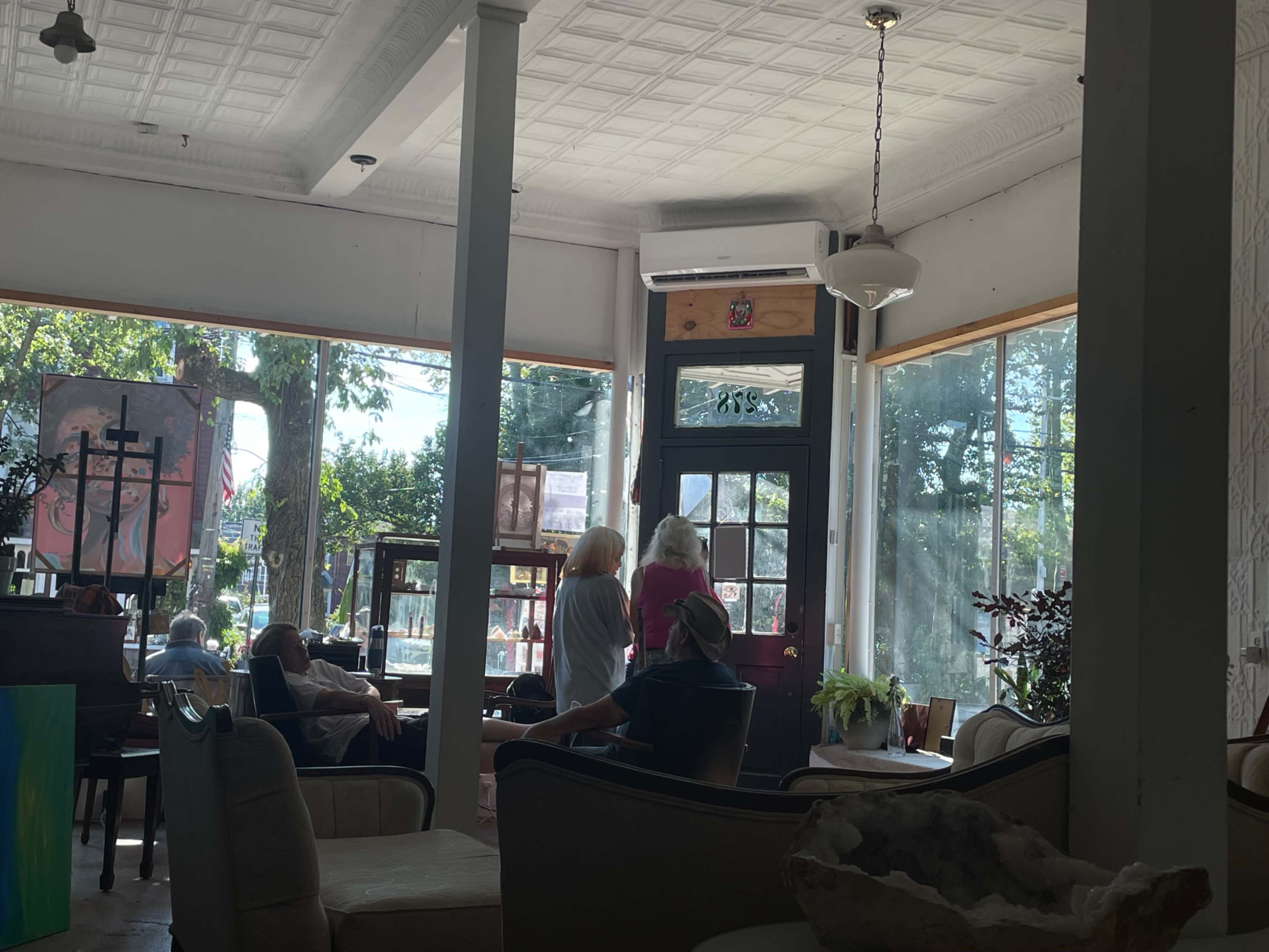 The image shows a cozy café with large windows, tables, and several people engaging in conversation.