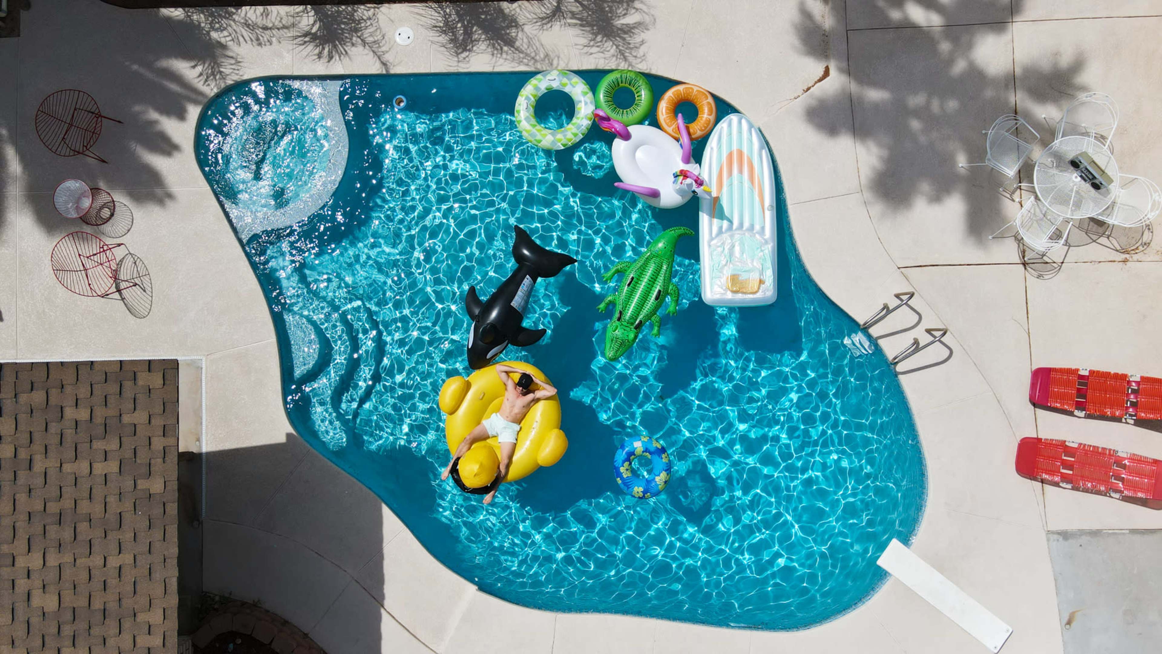 Aerial view of a swimming pool filled with various inflatable floats and a person lounging on a yellow float.