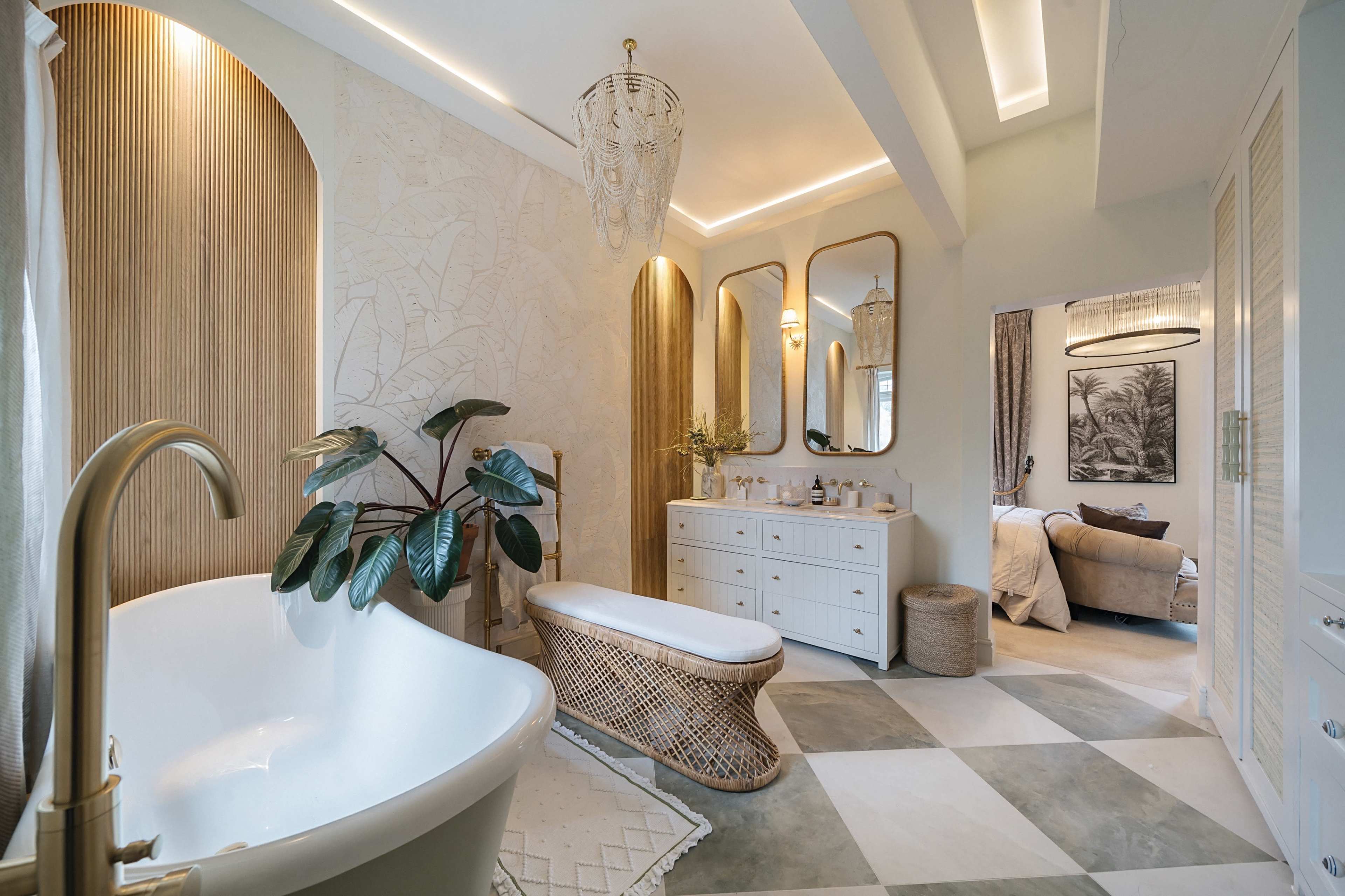 The image shows a modern bathroom featuring a freestanding bathtub, a woven bench, and a series of mirrors above a dresser, complemented by potted plants and neutral-toned decor.