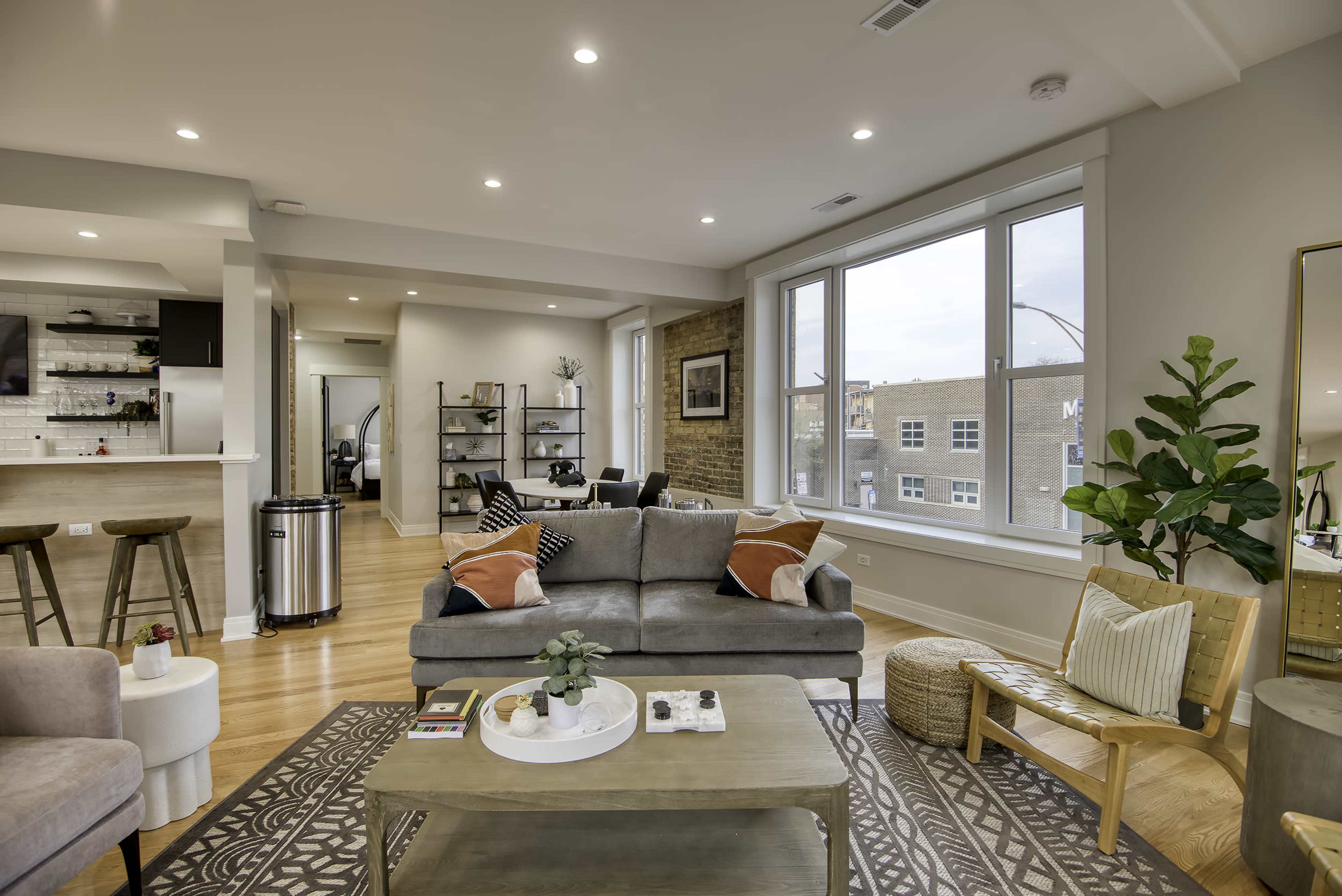 A modern living room with a gray sofa, a wooden coffee table, and large windows that let in natural light.
