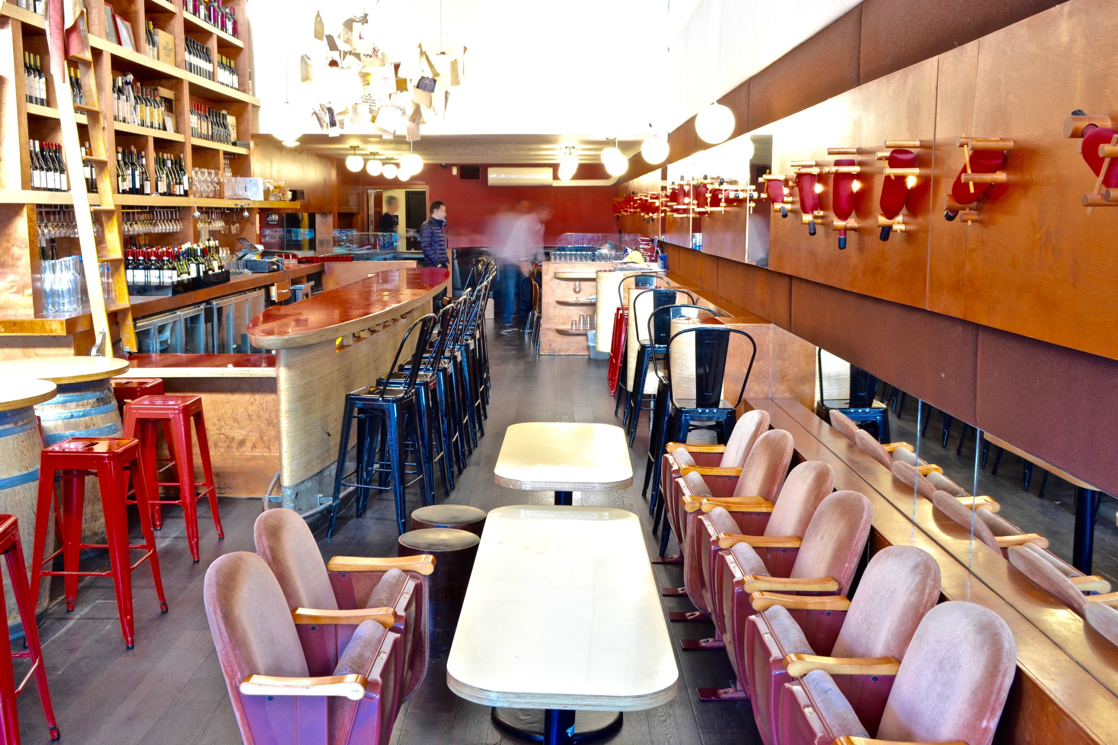 A modern bar and dining area with wooden furniture, red accents, and a long counter lined with bottles.