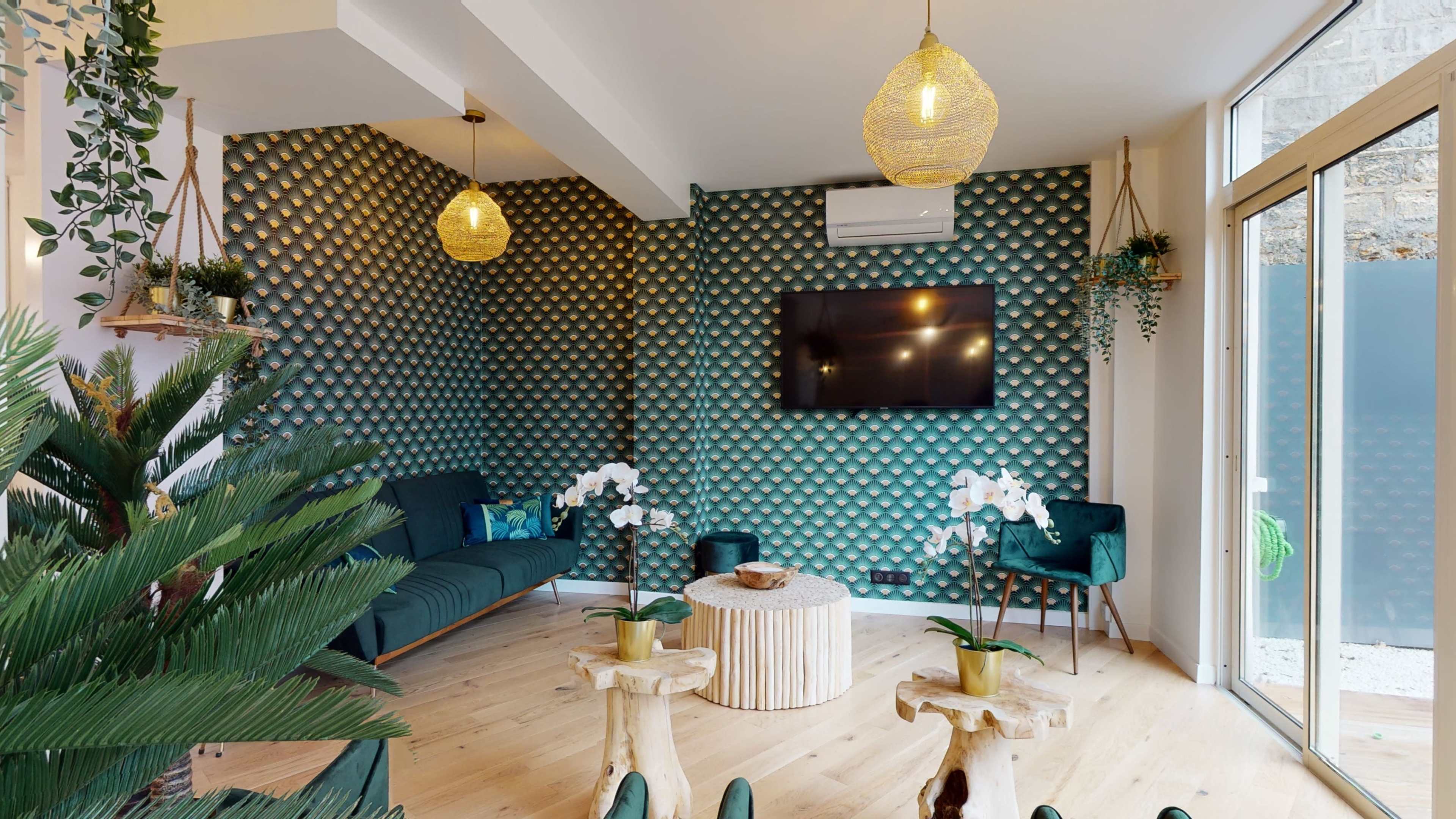 A modern living room featuring a textured green feature wall, a television mounted on the wall, a dark sofa, a round wooden coffee table, and decorative plants.