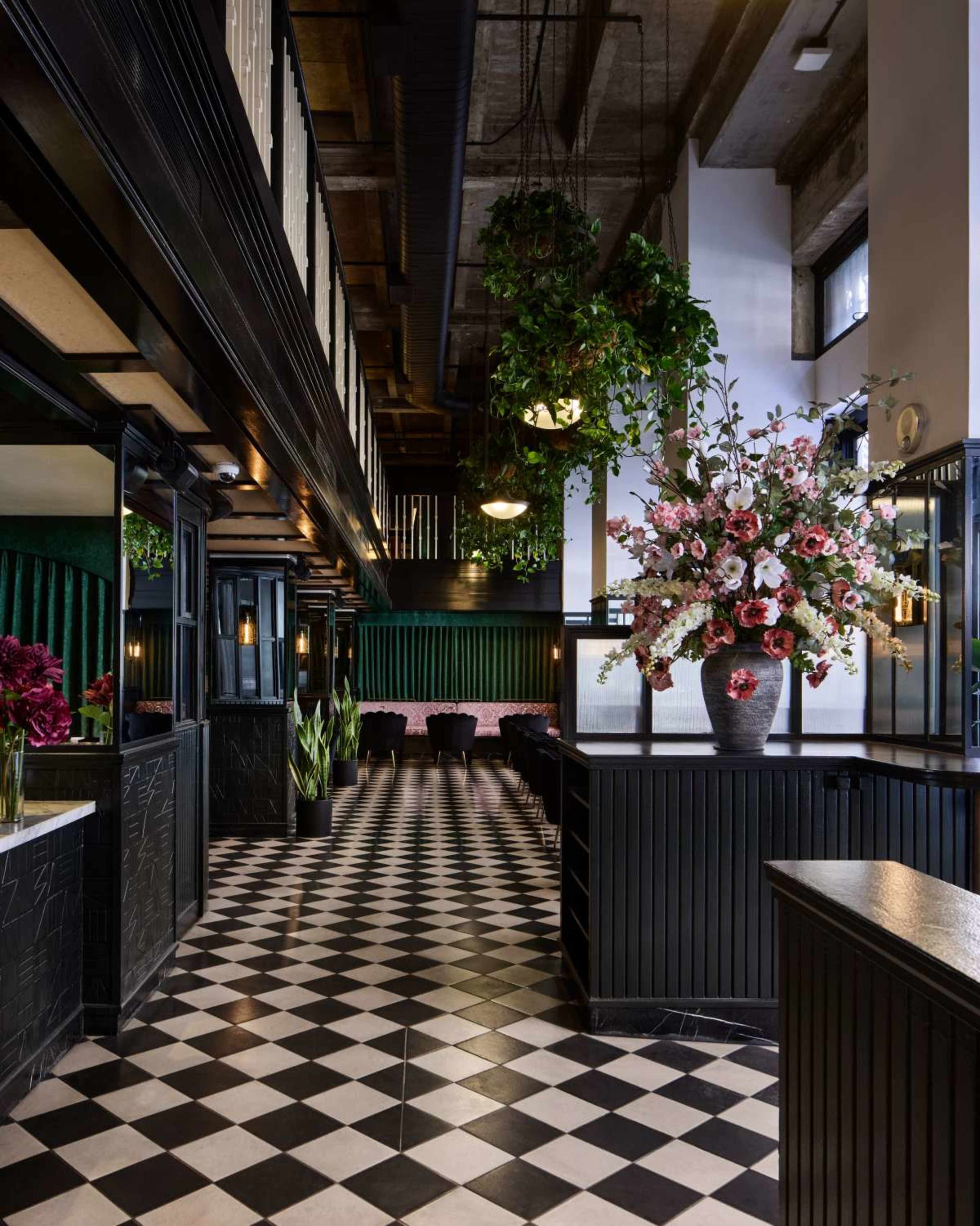 The image depicts a stylish restaurant interior featuring black and white checkered flooring, lush greenery, and elegant floral arrangements.