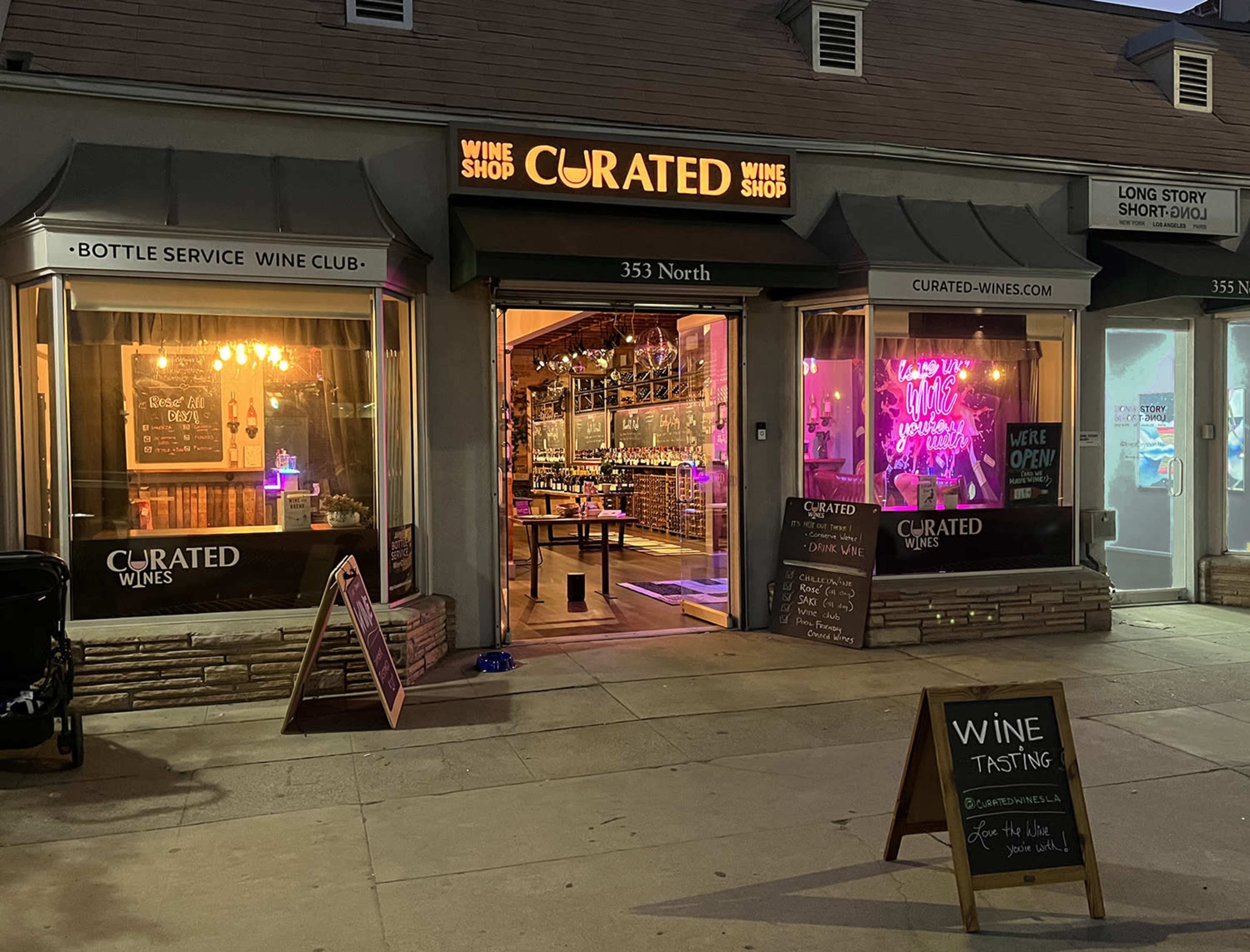 The image shows a wine shop with illuminated signage and a welcoming entrance showcasing wine bottles and a tasting area.