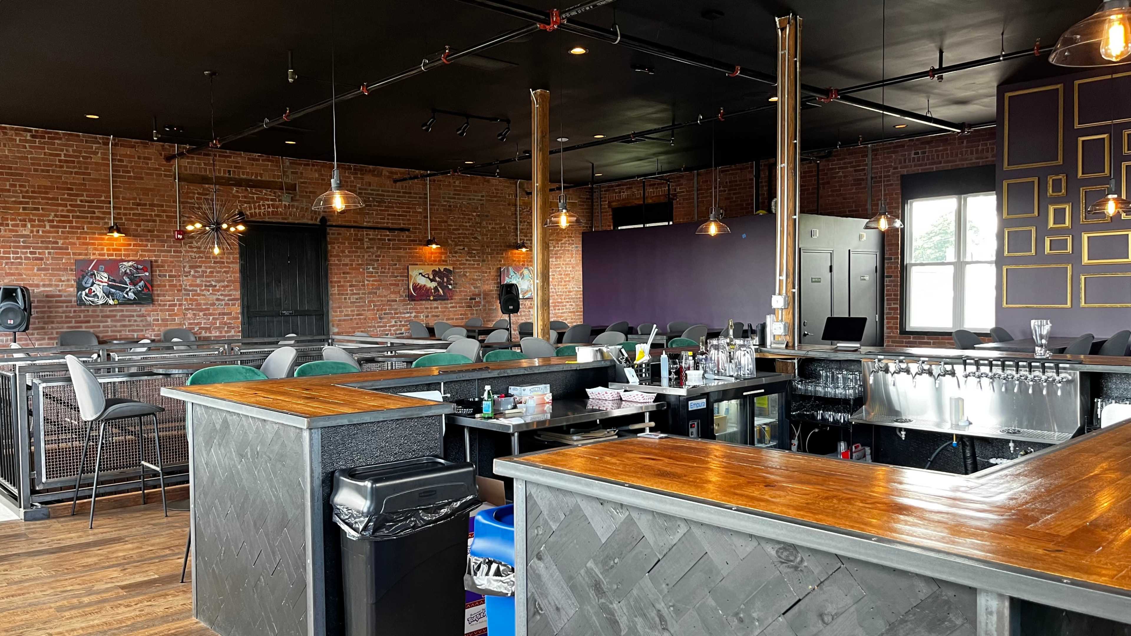 The interior of a bar with wooden counters, exposed brick walls, and rows of seating arranged in a casual layout.