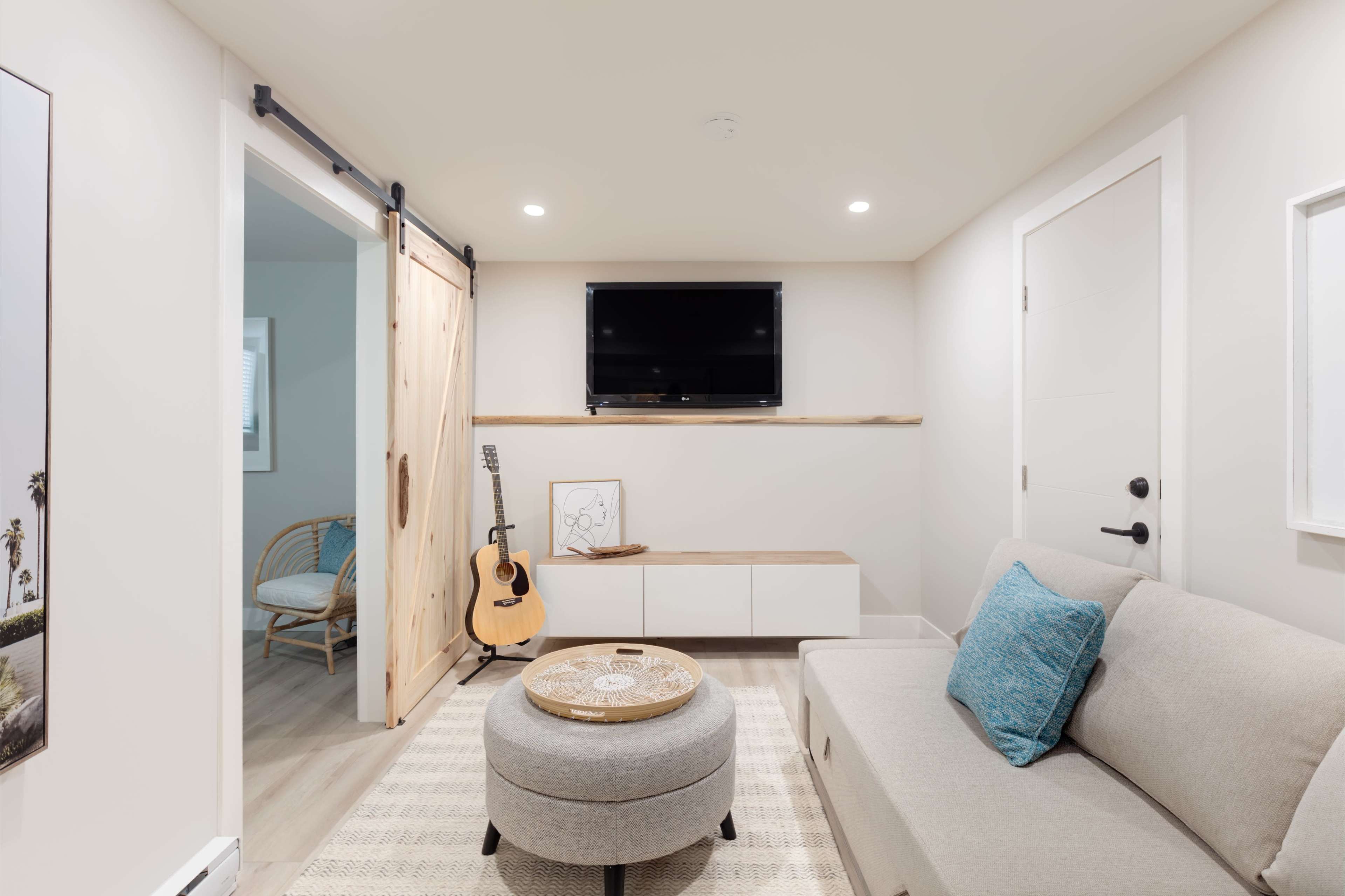 A cozy living area features a light-colored sofa, a round ottoman, a wall-mounted TV, and a sliding barn door leading to another room.