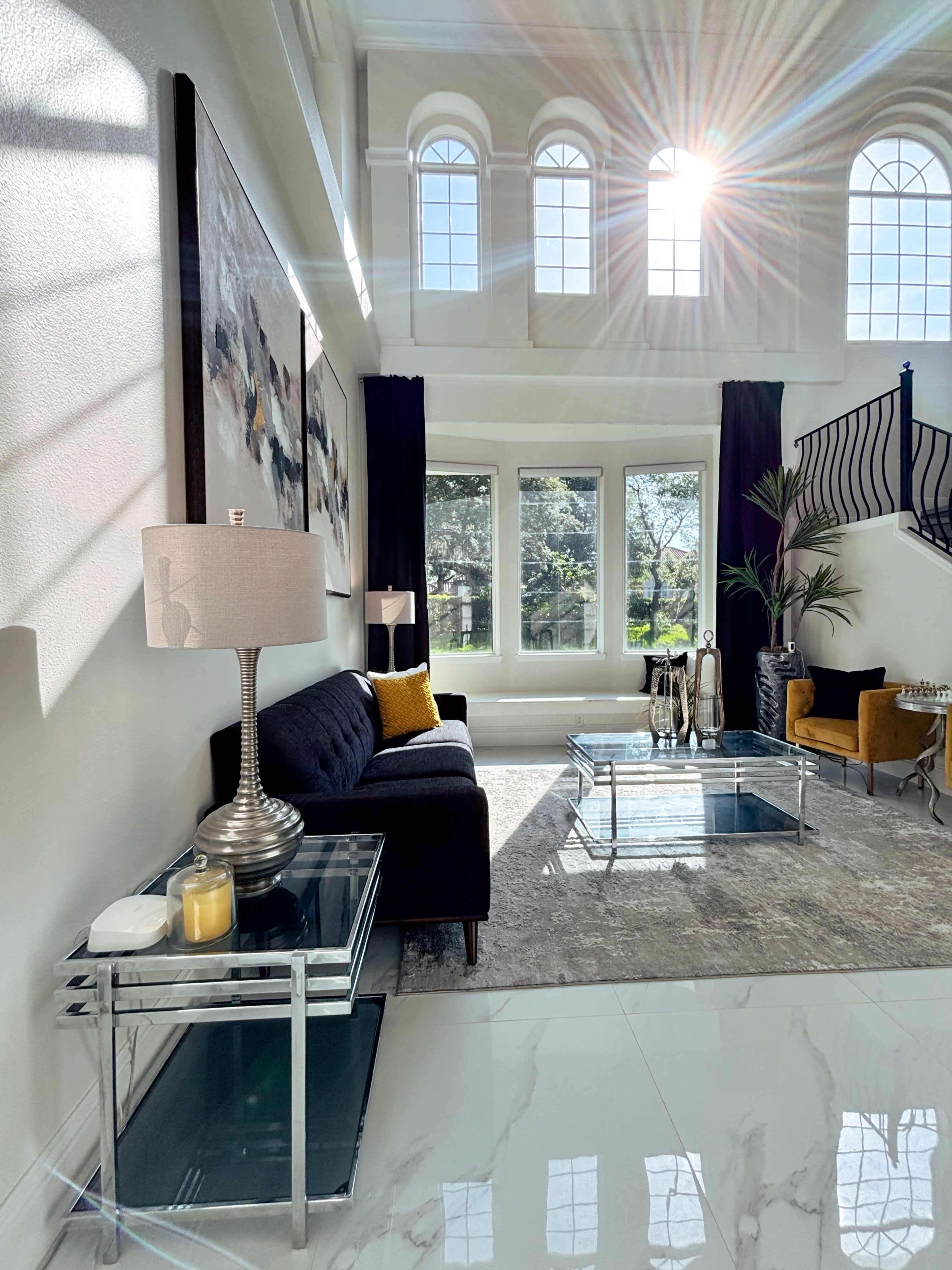 A bright living room features large windows, modern furniture, and decorative elements on a marble floor.