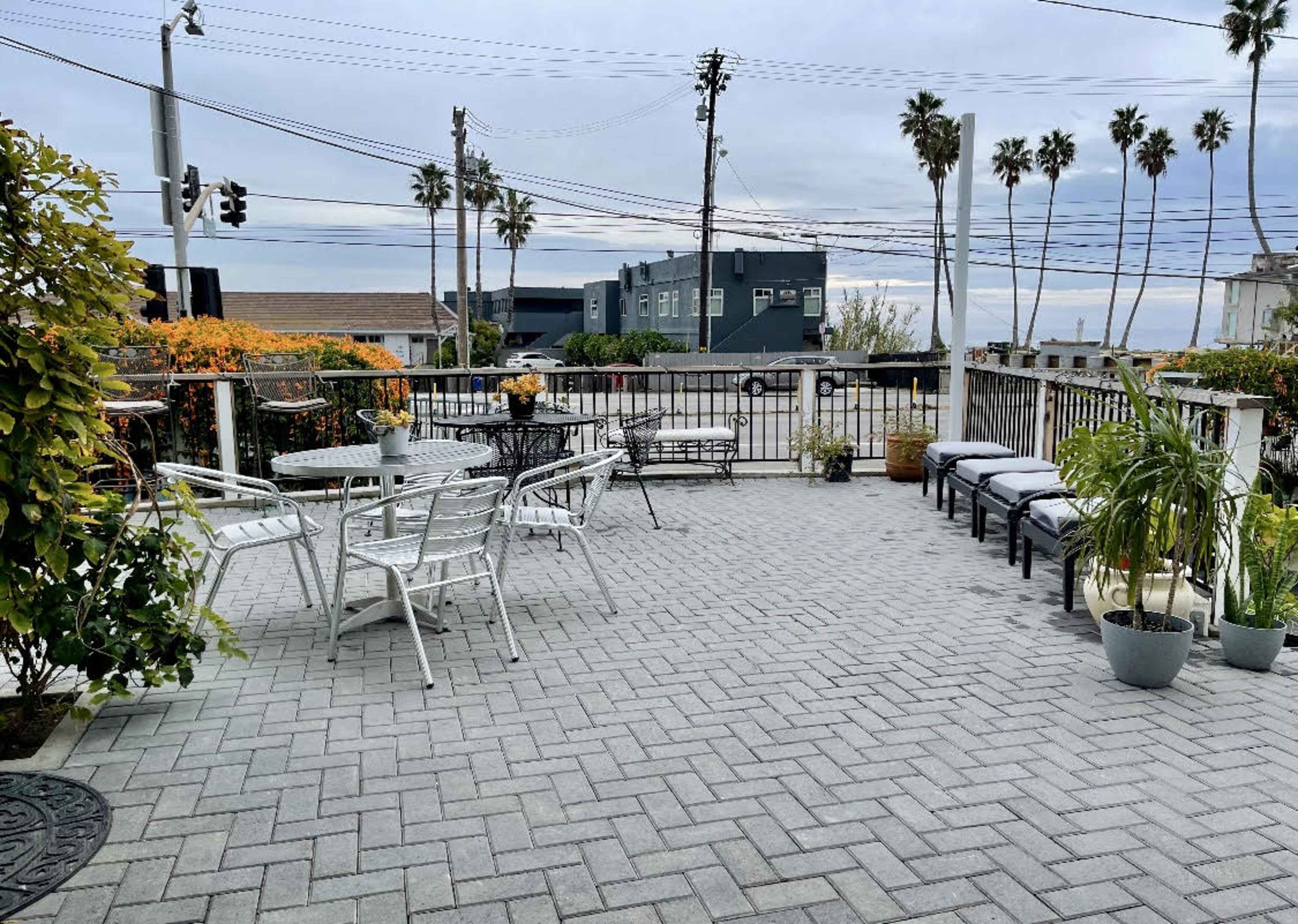 The image shows a terraced outdoor space with patio furniture, potted plants, and a view of palm trees in the background.
