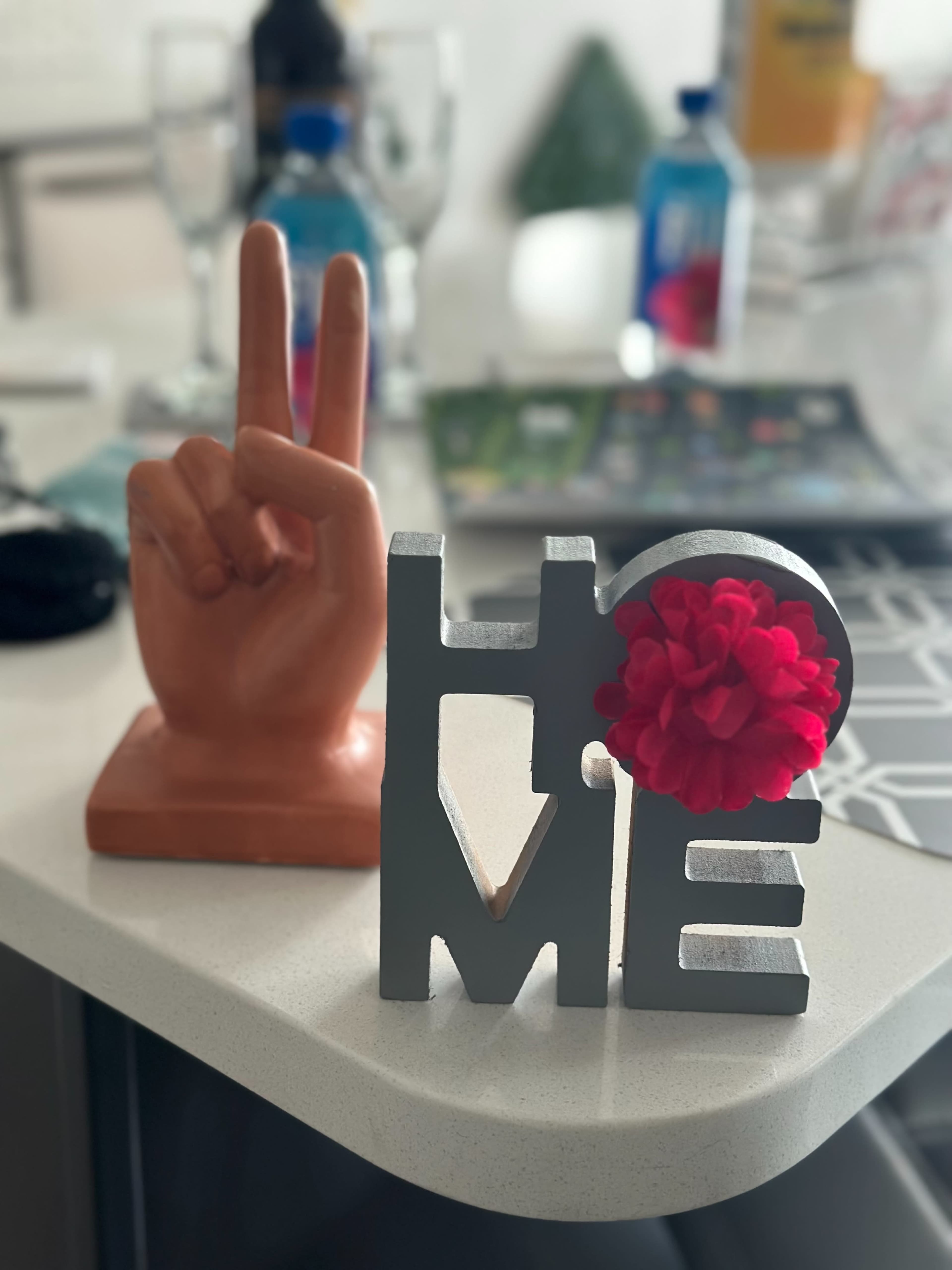 A hand-shaped sculpture making a peace sign beside a decorative sign that spells "HOME" with a red flower attached.