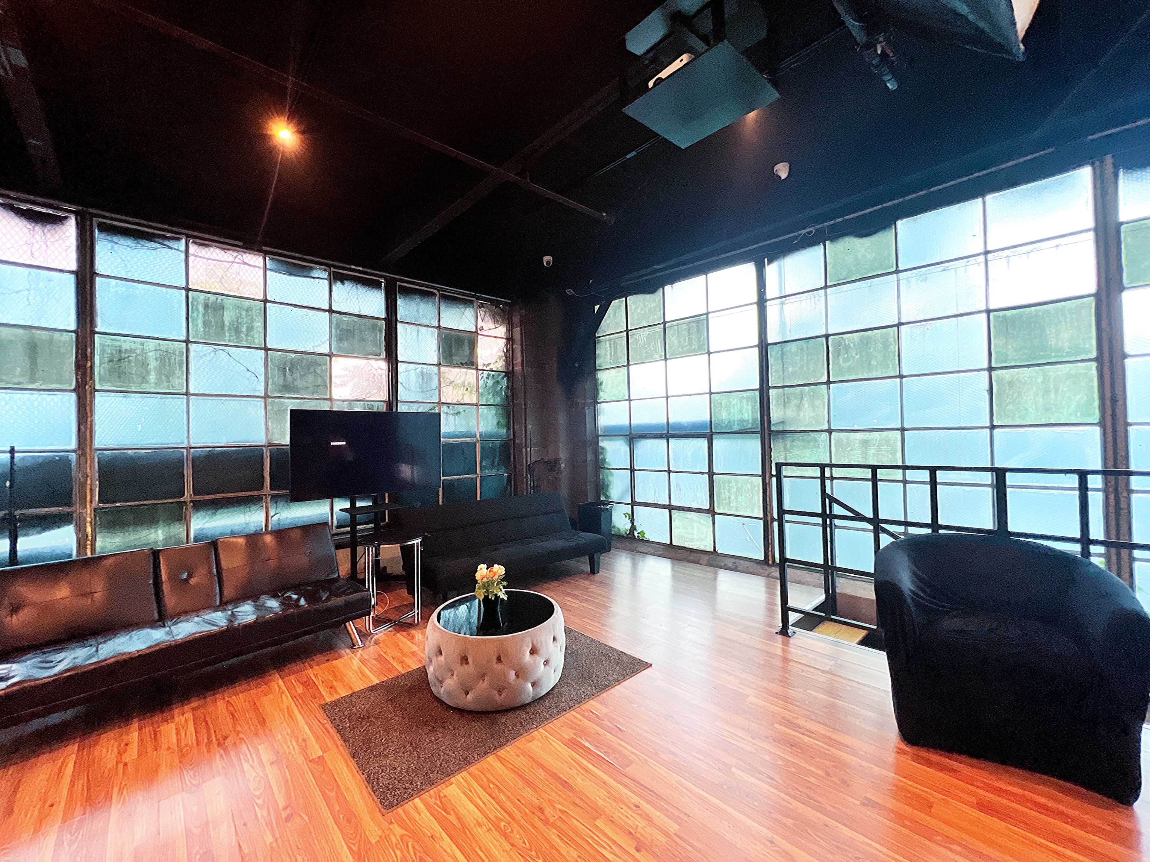 A spacious room with large windows, dark walls, wooden flooring, and contemporary furniture, including a black sofa, a round coffee table, and a television.