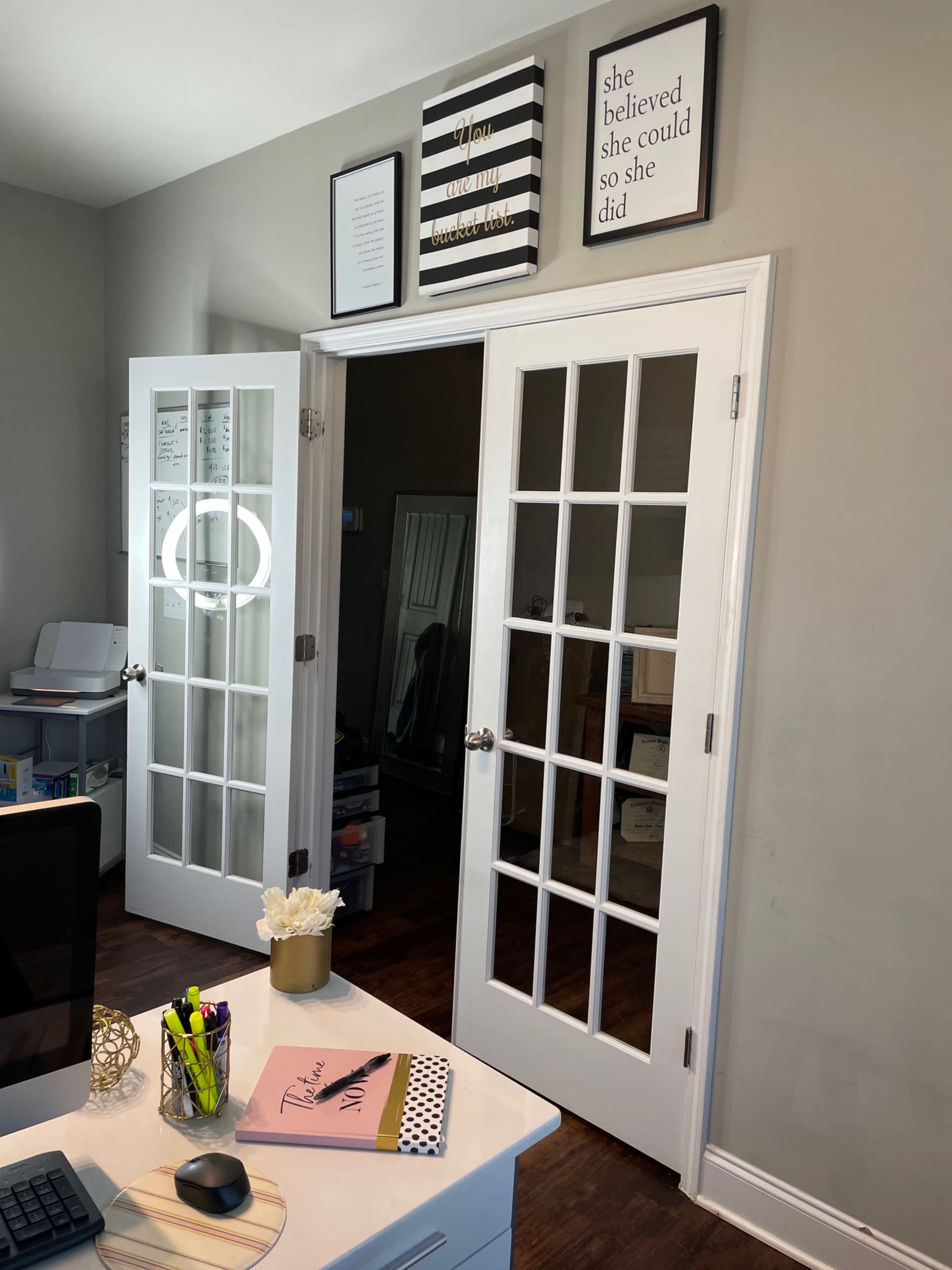 An office space with French doors leading to another room, a modern desk with a computer, and framed artwork on the wall.