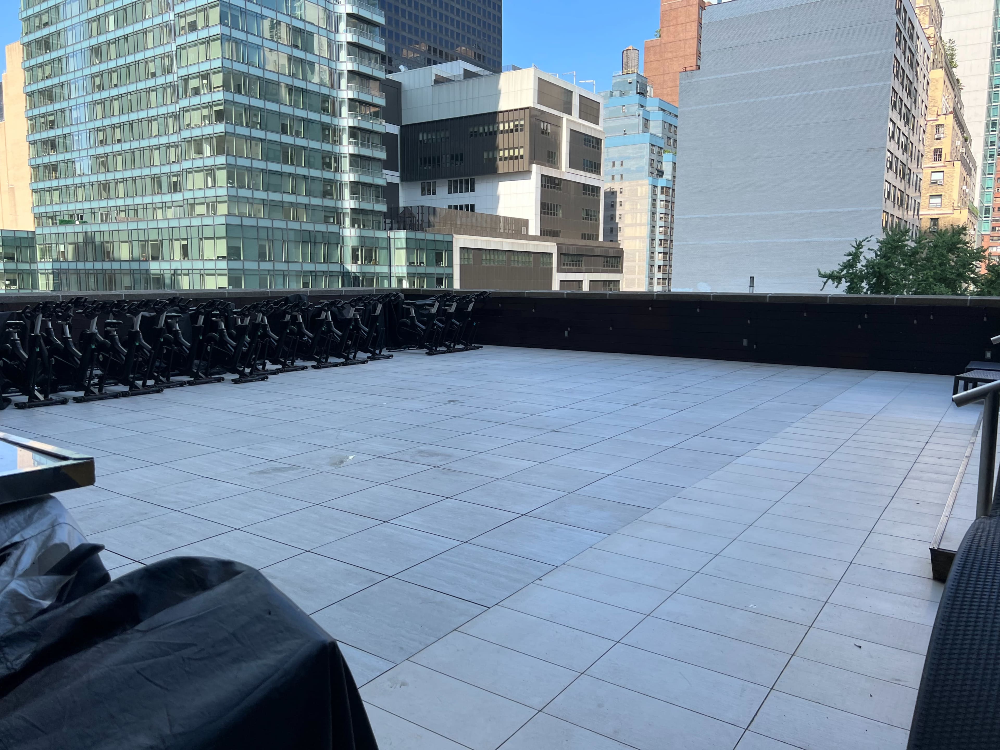 The image shows a spacious rooftop terrace with a tiled floor and several rows of black chairs lined against a railing.