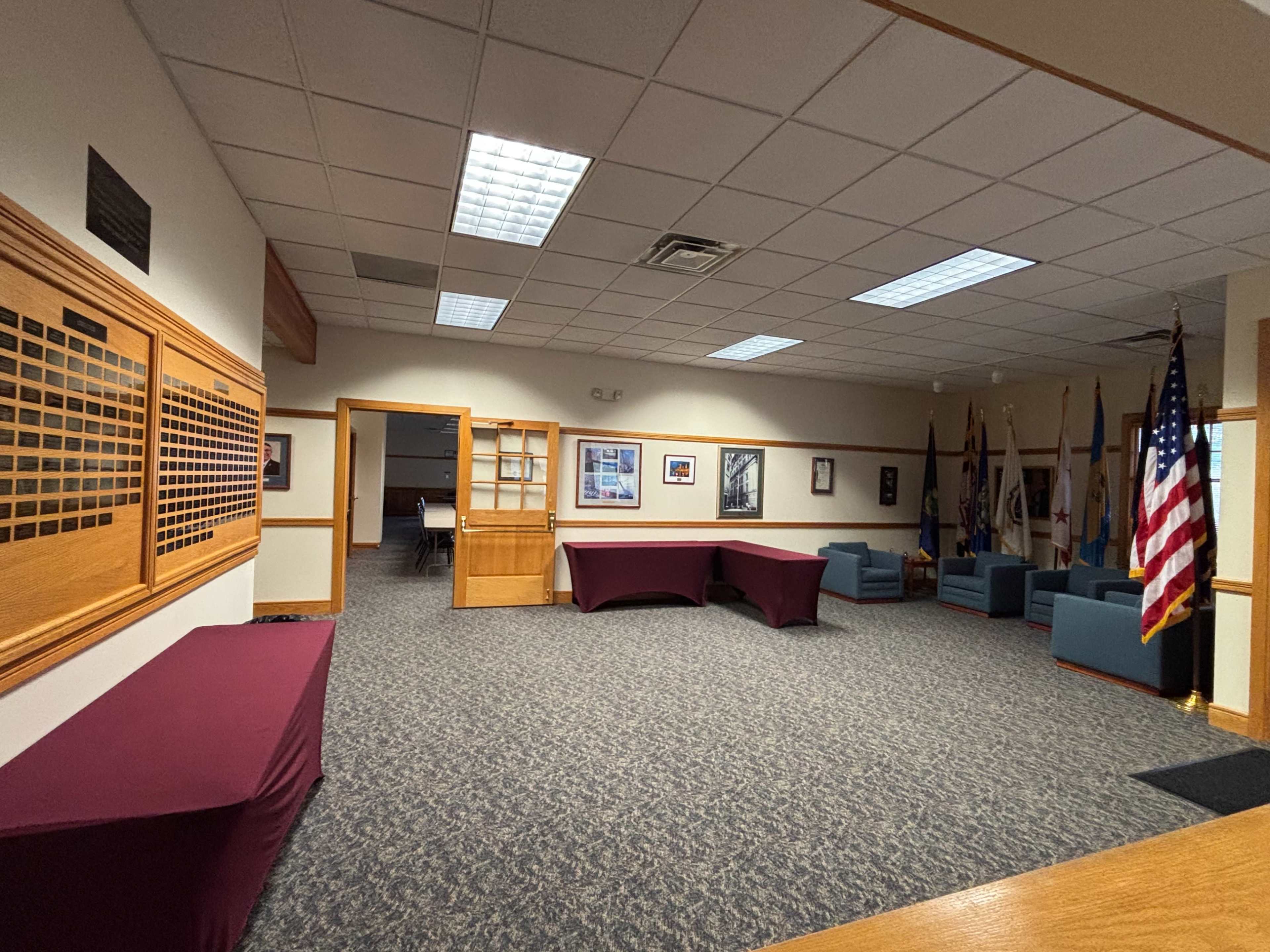 The image shows a spacious room with blue seating, a maroon tablecloth covering tables, and walls displaying framed photos and flags.