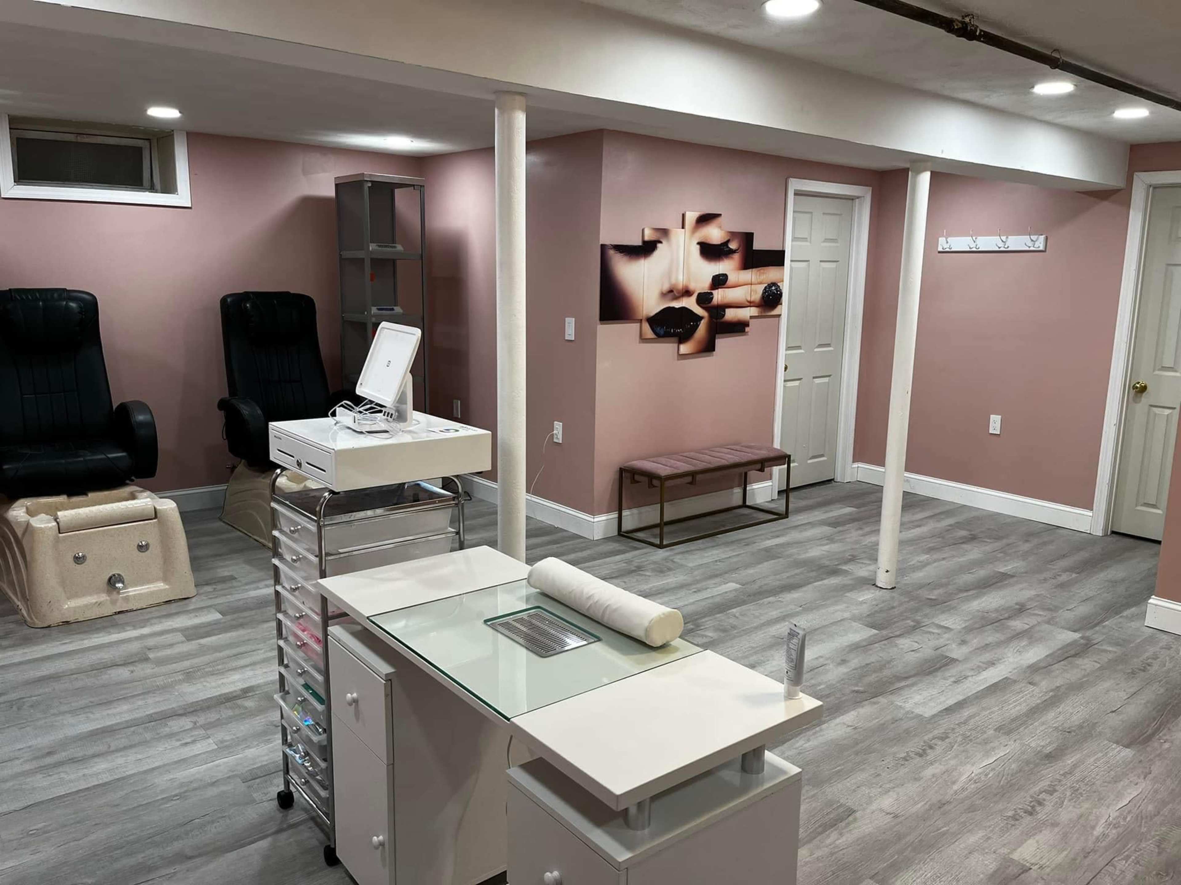 A finished basement with light pink walls, gray flooring, a reception area with a glass-top desk, and seating areas including two dark chairs and a bench.