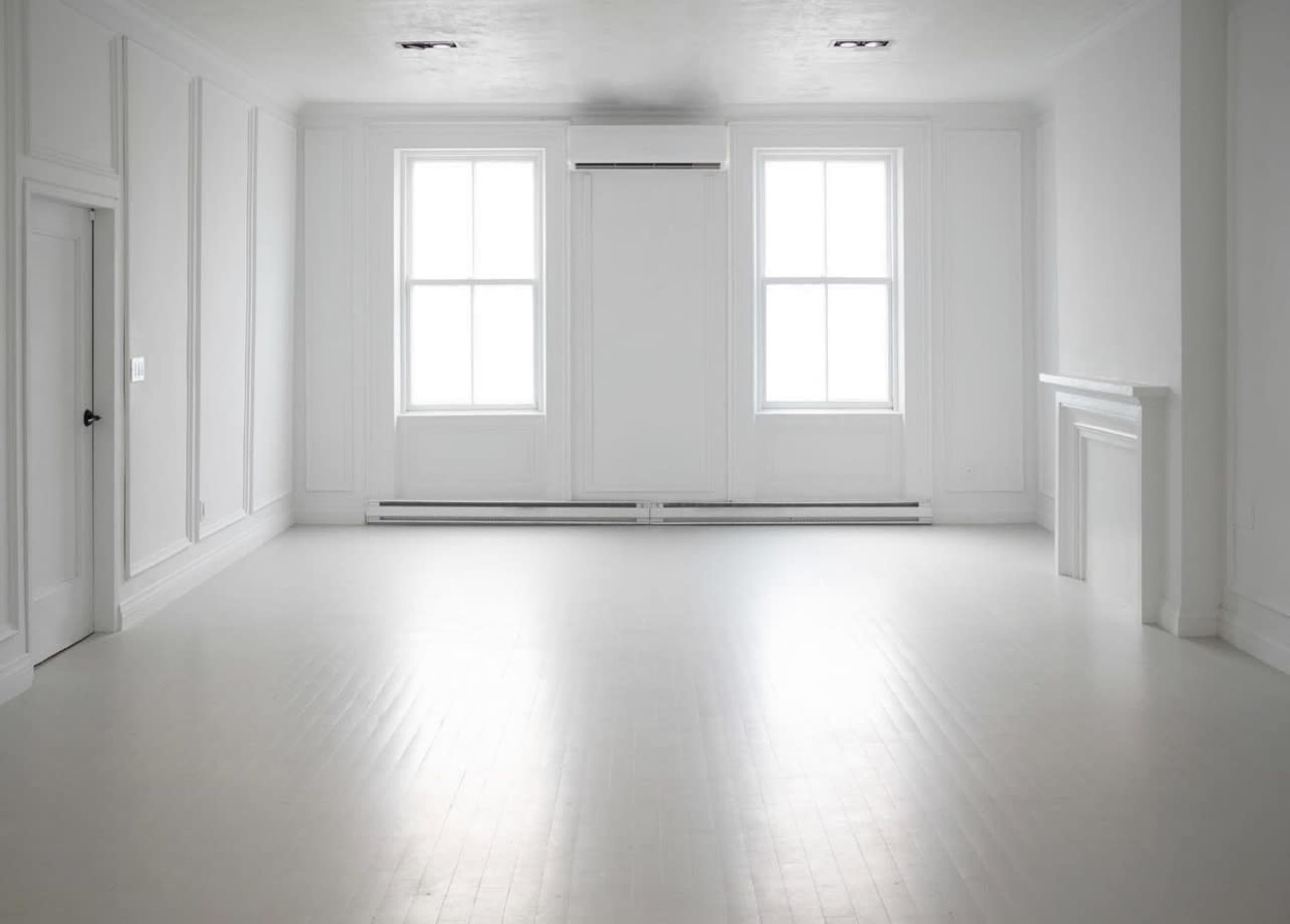 A bright, empty room with white walls, large windows, and a wooden floor.